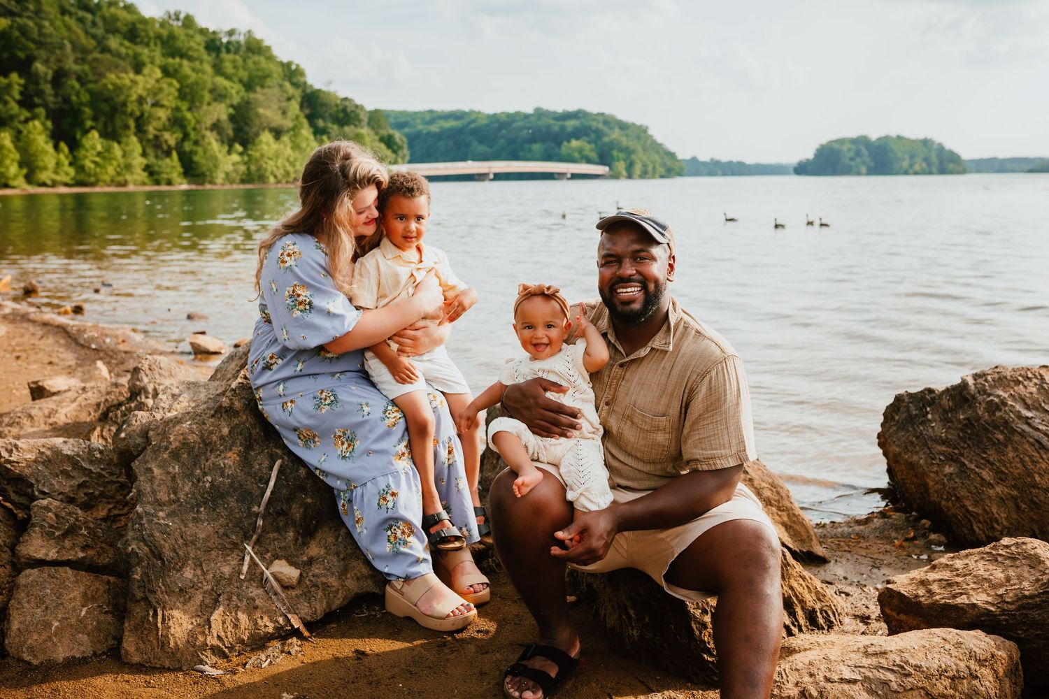 Happy interracial family of four sitting on rocks by a lake on a warm sunny day.