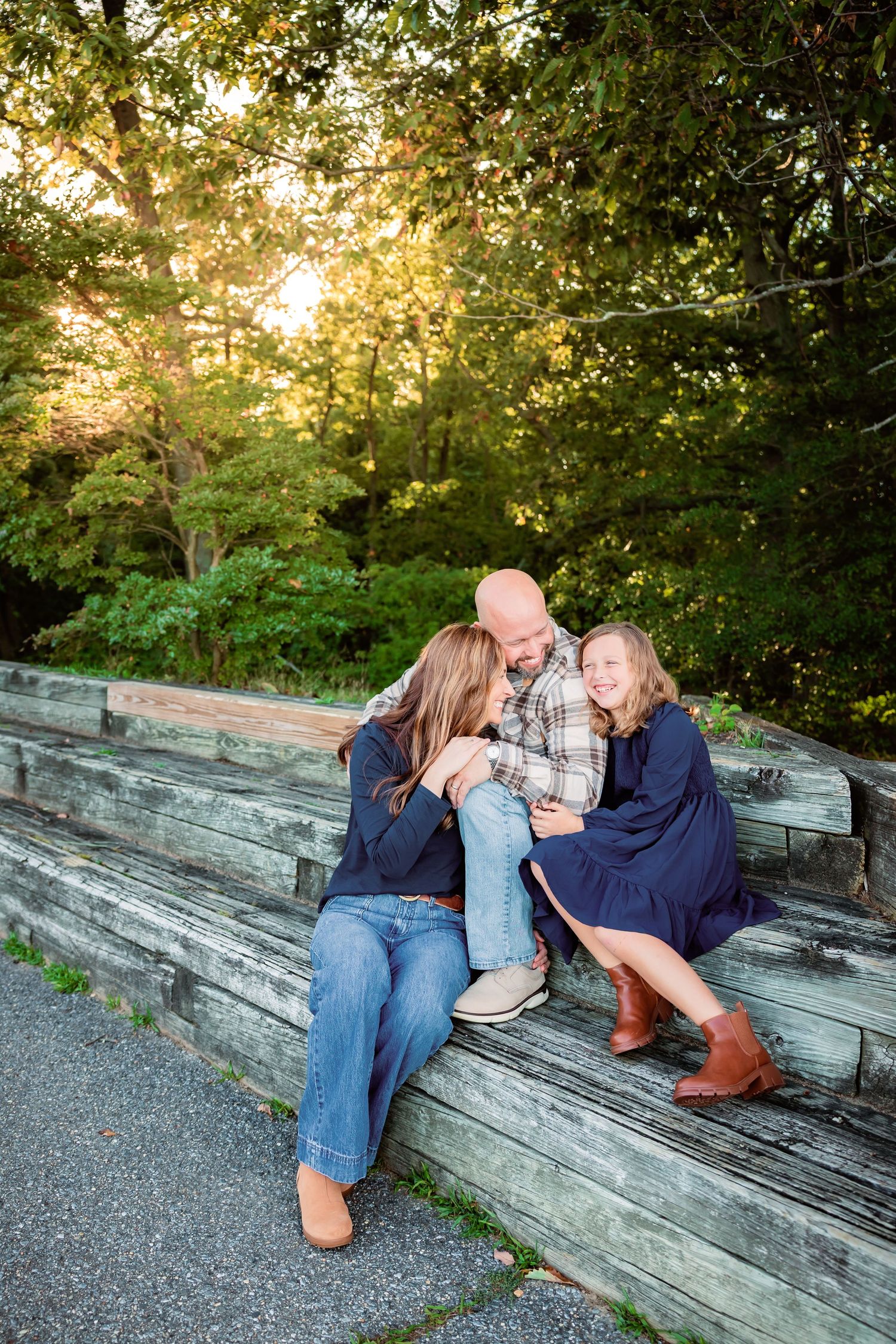 Father and two daughters sitting closely together on wooden bleachers, sharing a warm moment at sunset.