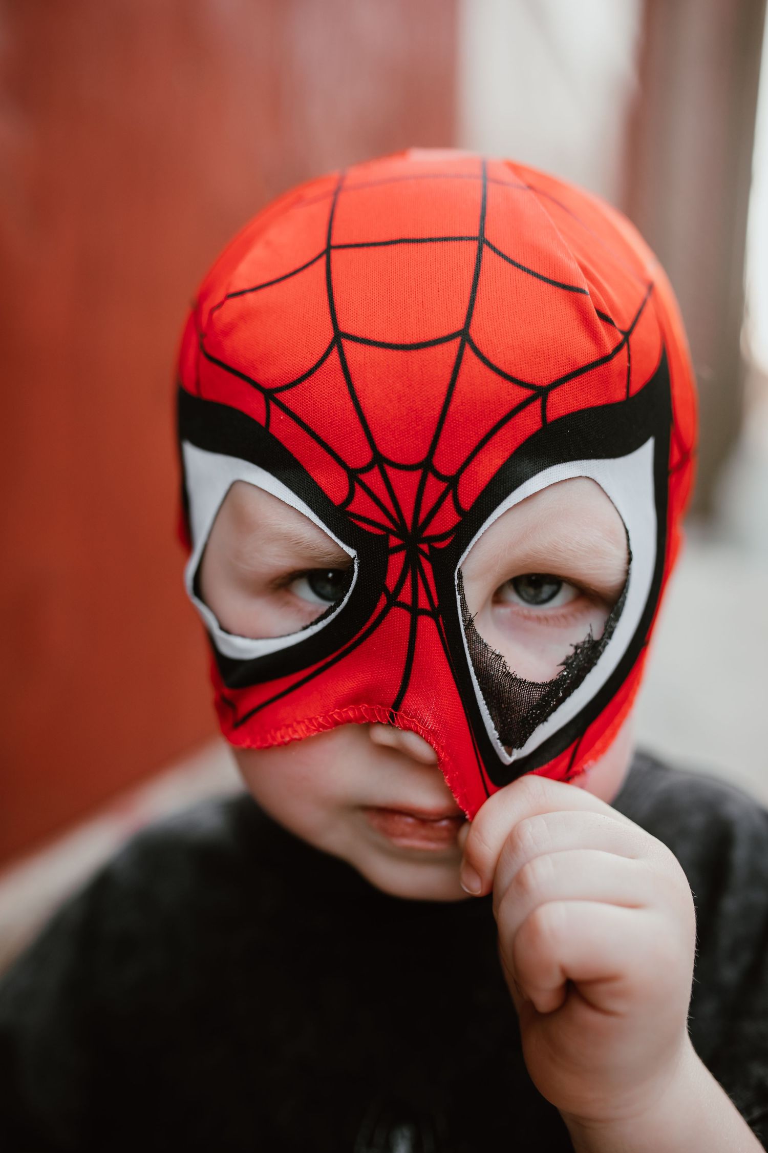 Young child wearing a red and black Spider-Man mask looking at the camera outdoors.