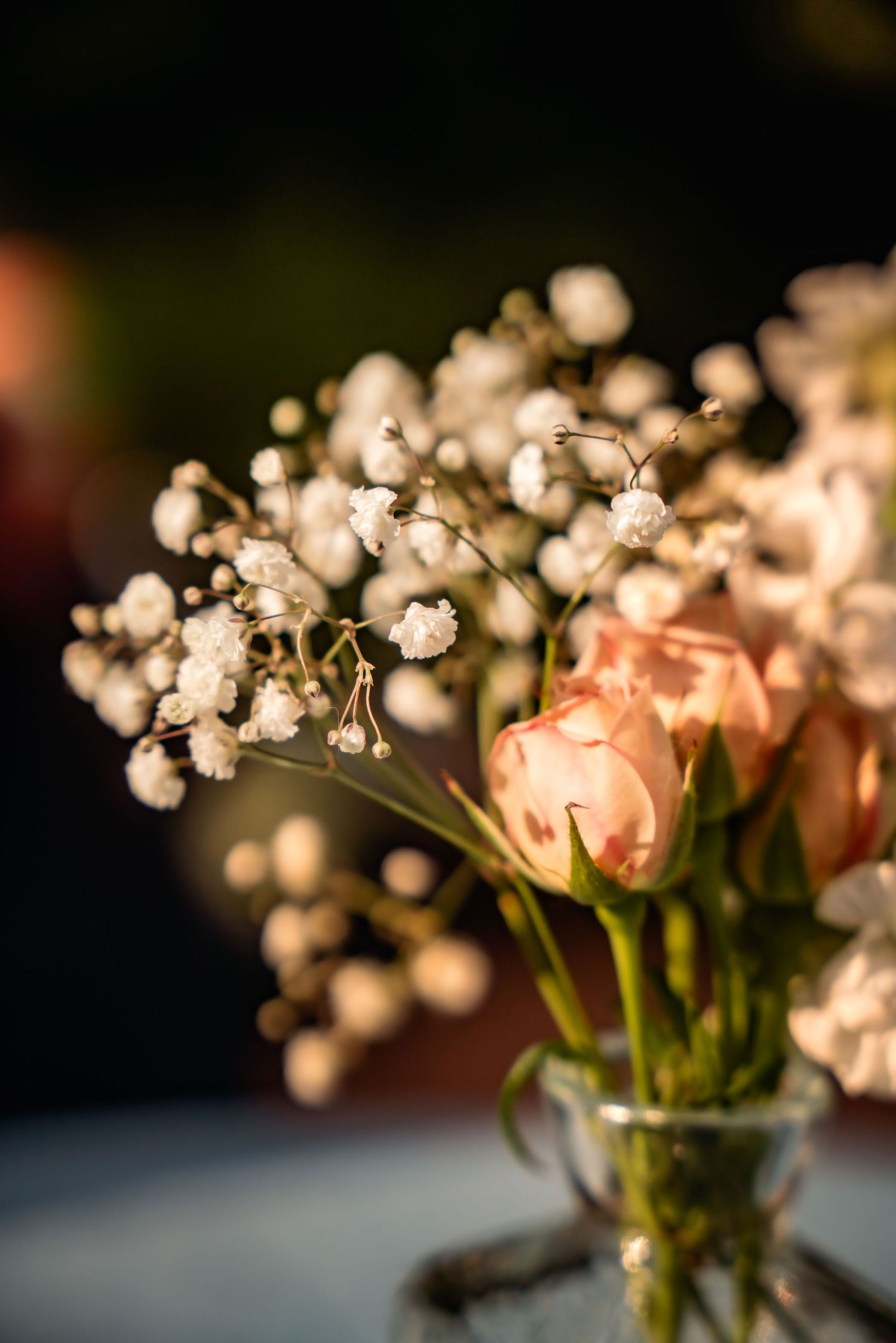 Elegant wedding centerpiece with pink roses and white baby's breath in a glass vase with warm golden light.