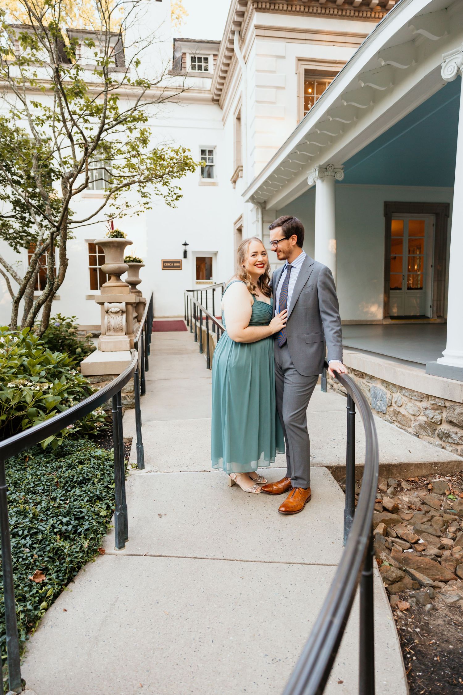 Couple in elegant attire smiling on steps outside a historic mansion.
