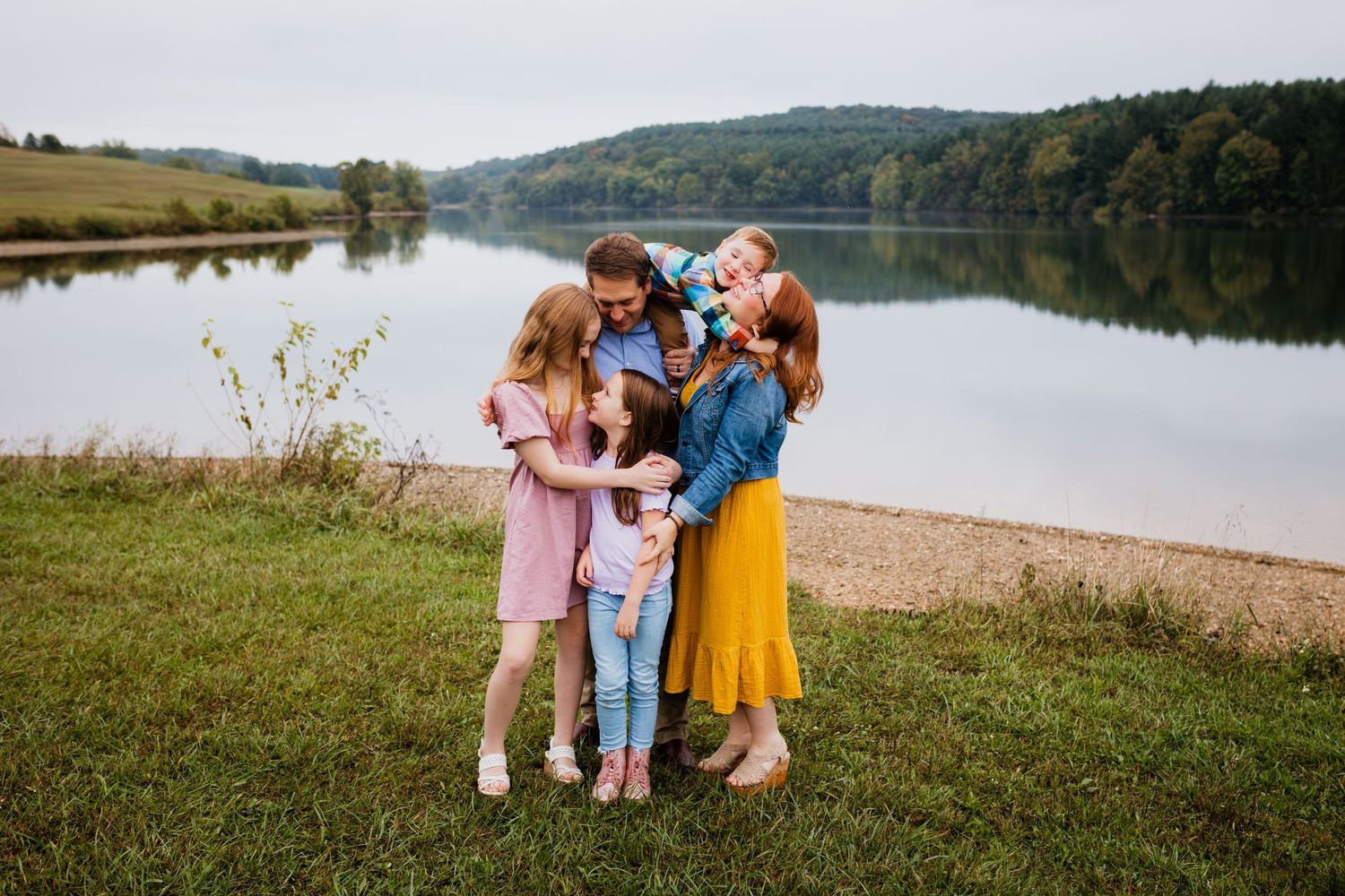 A joyful family of five shares a warm embrace near a peaceful lakeside setting.