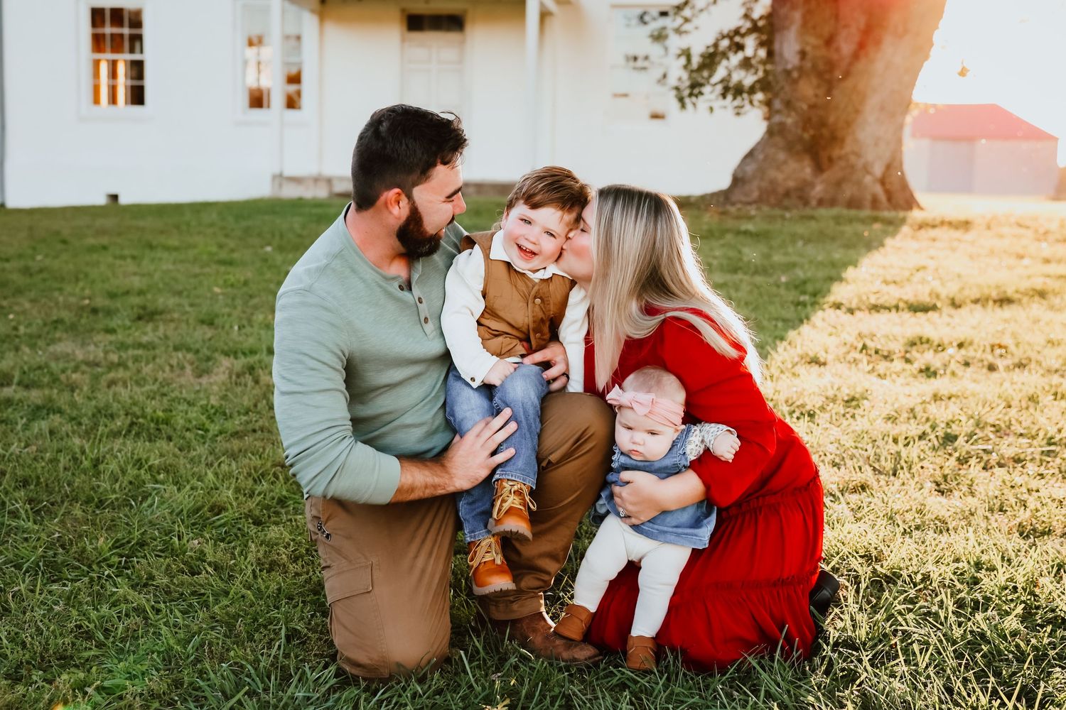 Loving family of four with two young children sharing a joyful moment on green lawn.