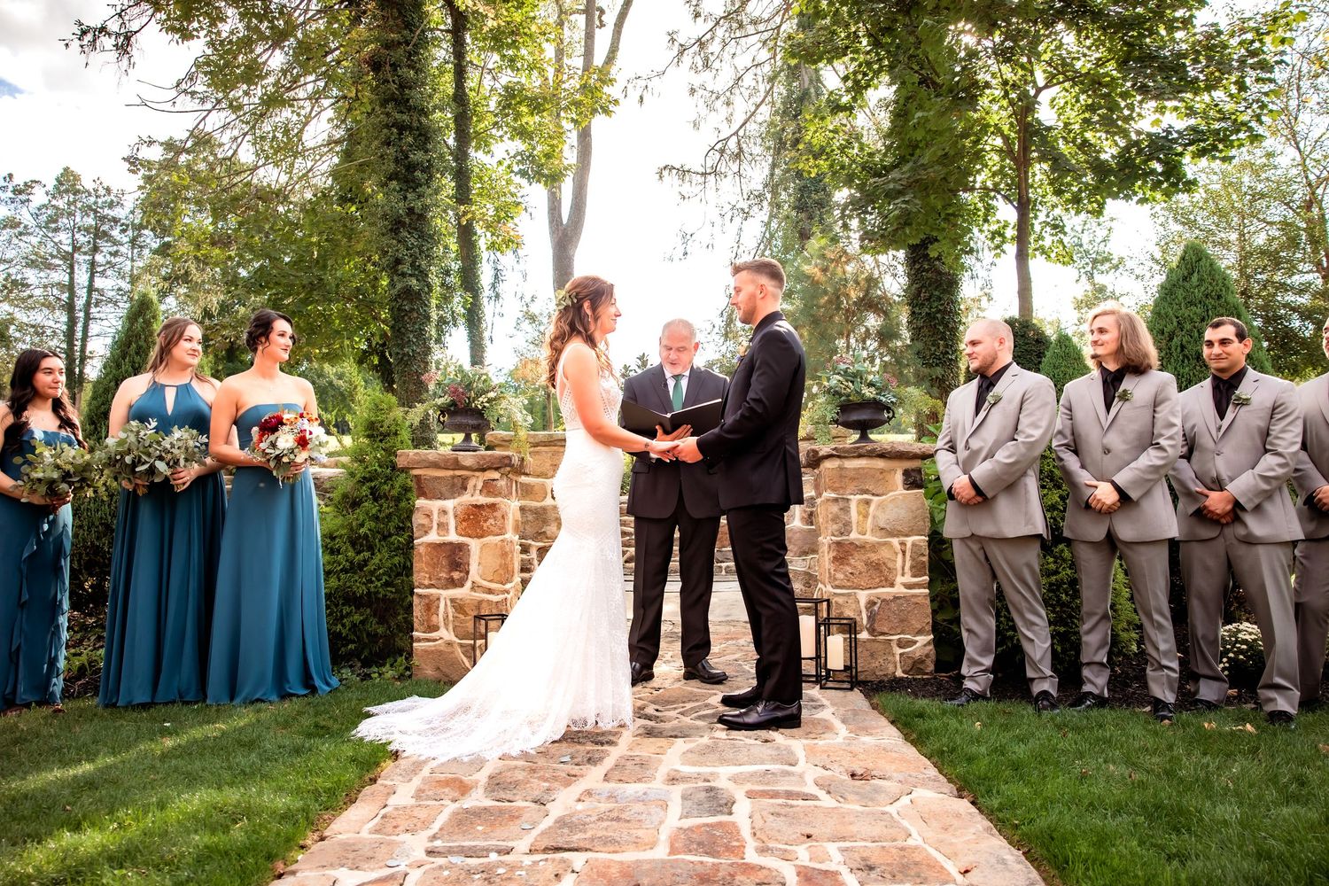 Couple exchanging vows at an outdoor stone garden wedding ceremony with bridal party.