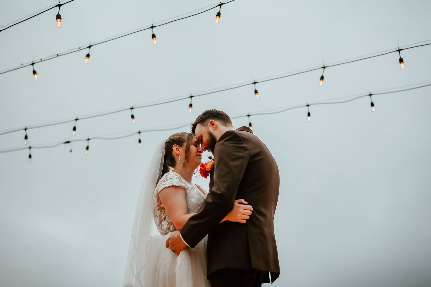 Bride and groom sharing a romantic kiss under string lights at outdoor fall wedding ceremony.