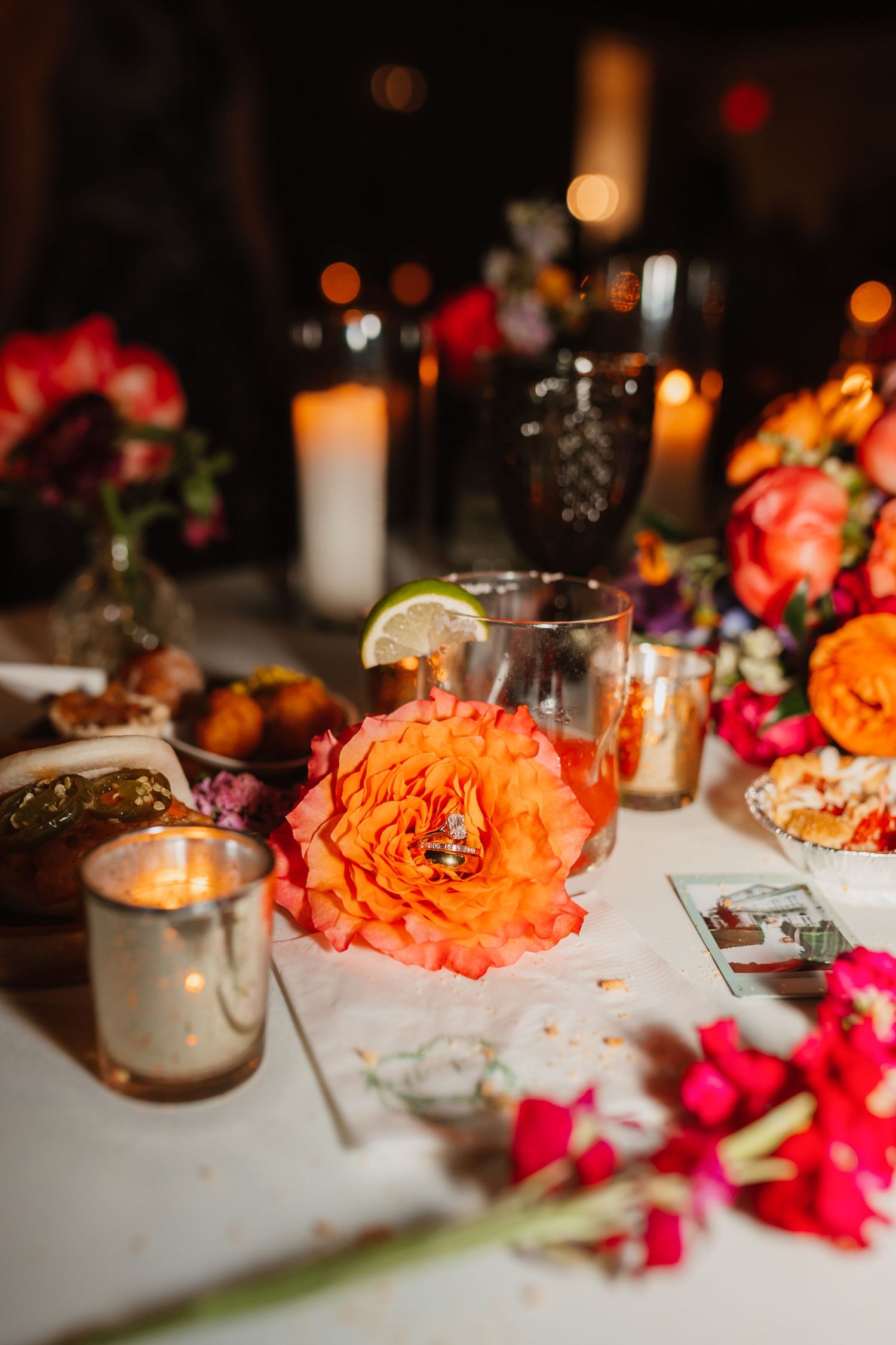 Romantic wedding reception table with orange roses, candles, and vibrant floral centerpieces in warm lighting.
