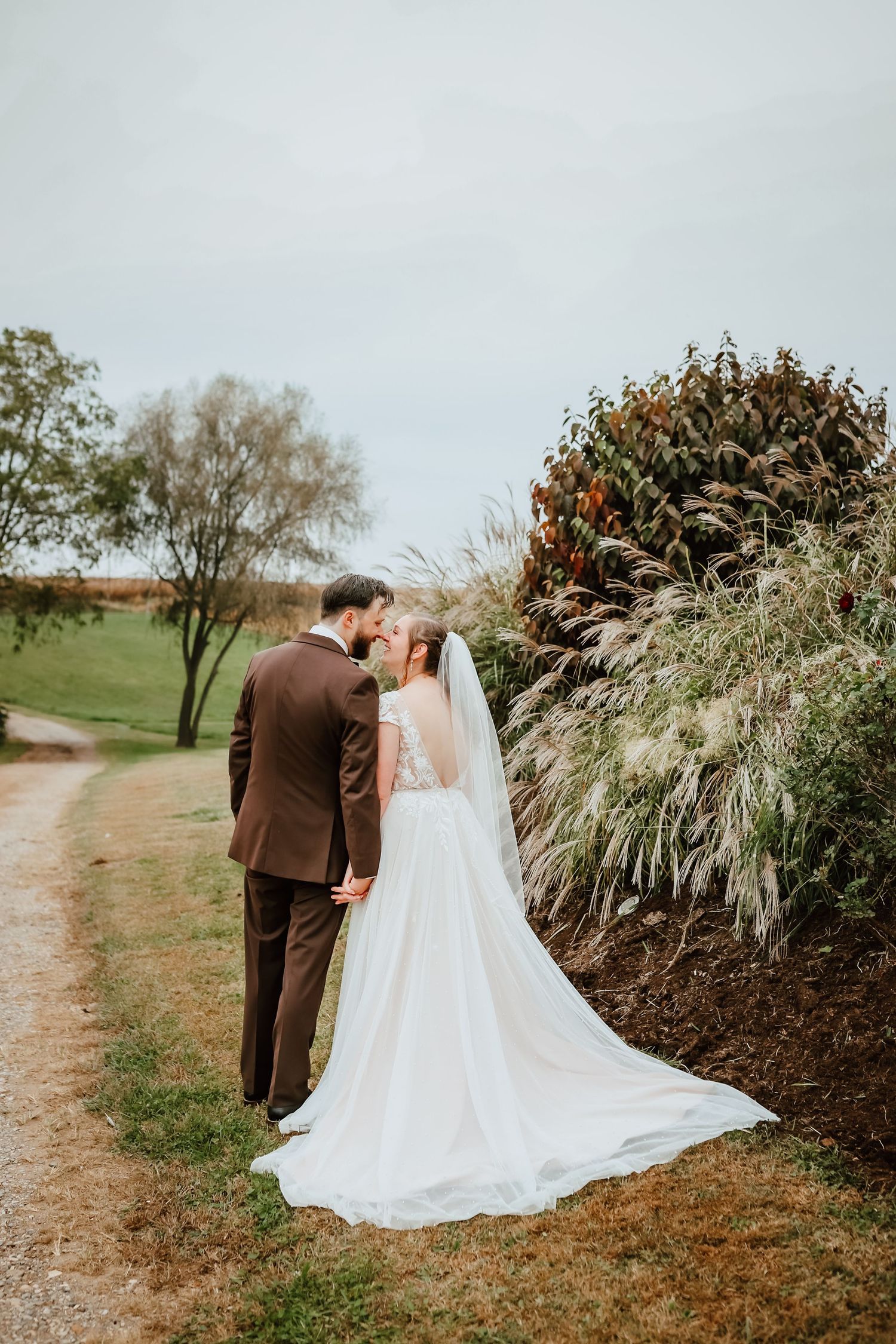 Bride and groom kissing near colorful autumn foliage along a rustic dirt path.
