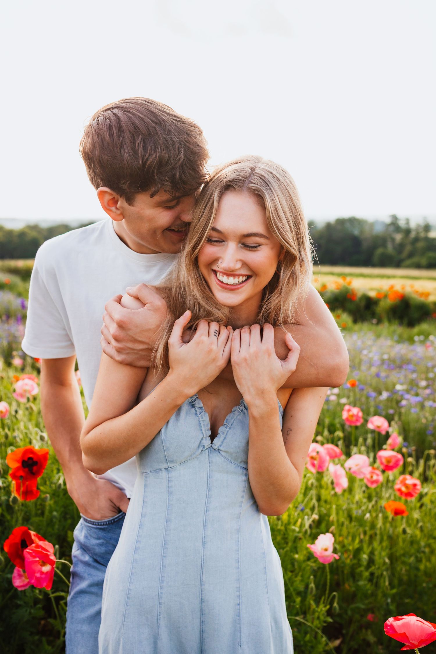 Happy couple embracing in vibrant poppy flower field at sunset.