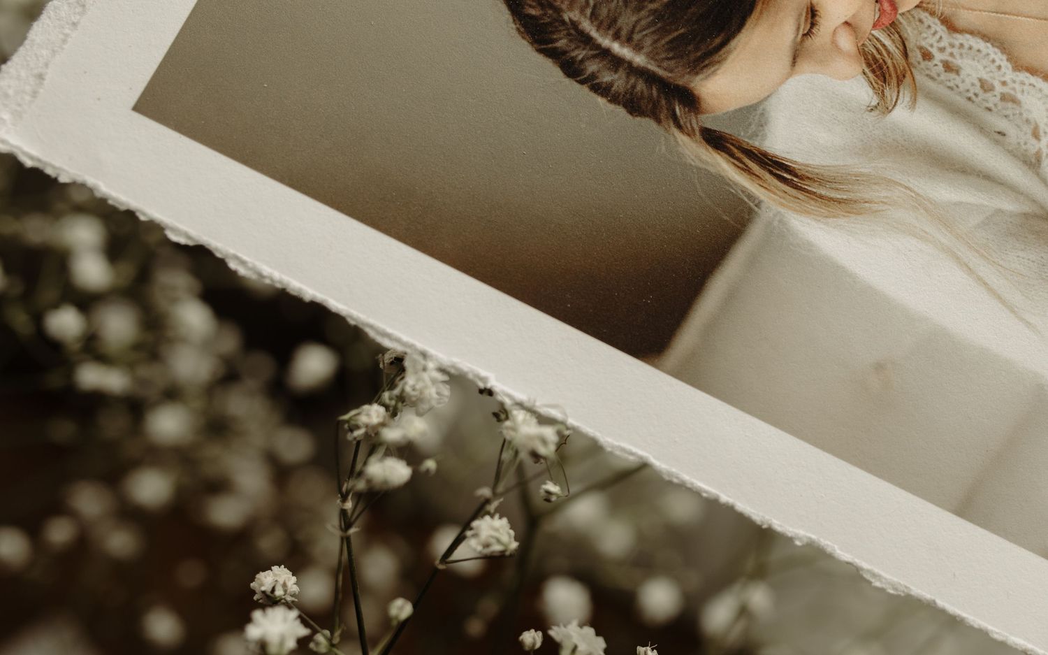Torn-edge photo print of a woman with a braid over dried white flowers in a soft, dreamy composition.