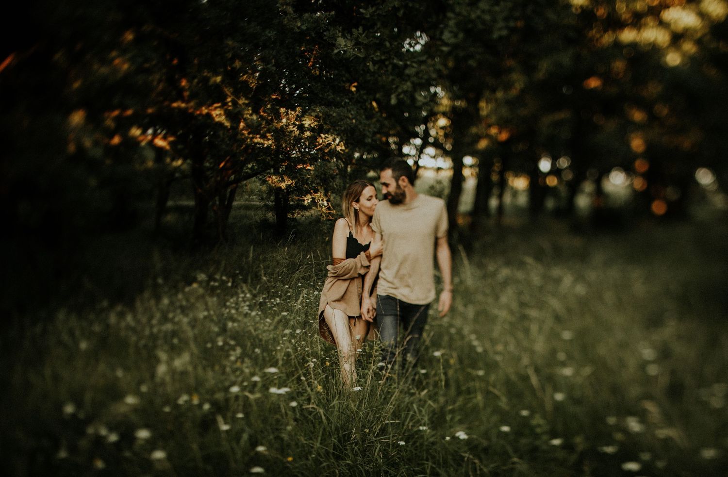 Couple strolling together through a wildflower meadow with warm, glowing autumn light filtering through the trees.