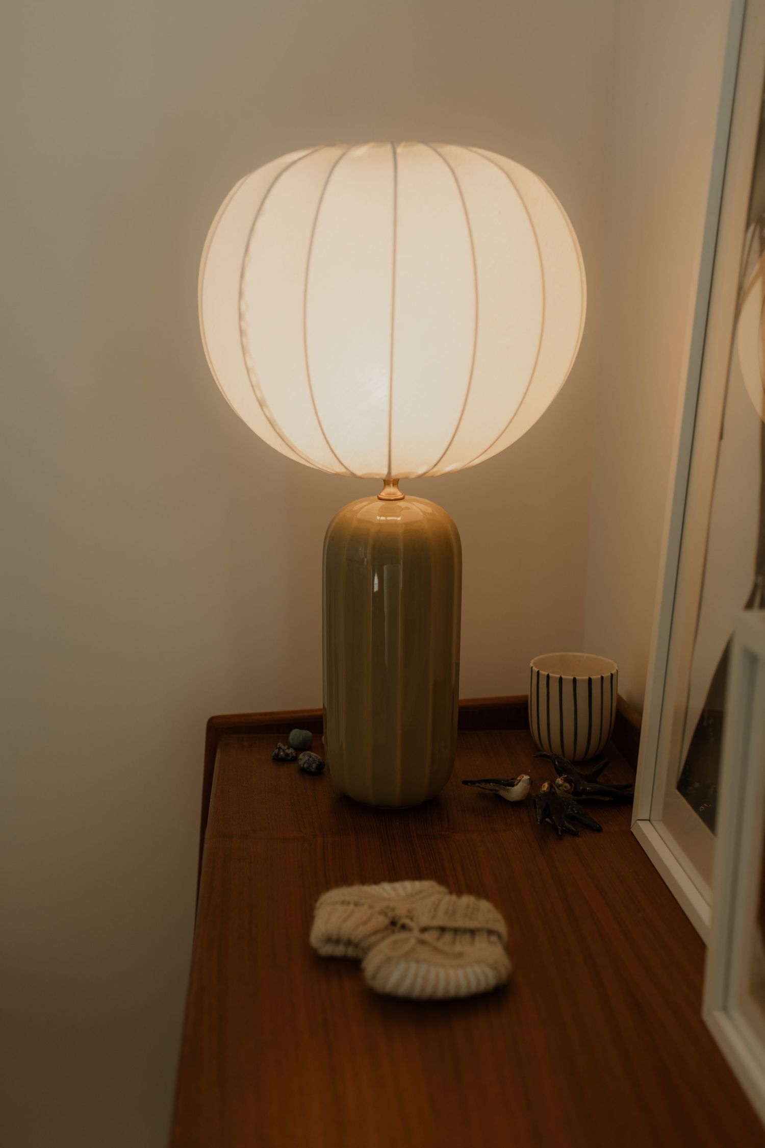 Glowing white table lamp on a wooden dresser beside tiny knitted baby booties in a softly lit nursery.