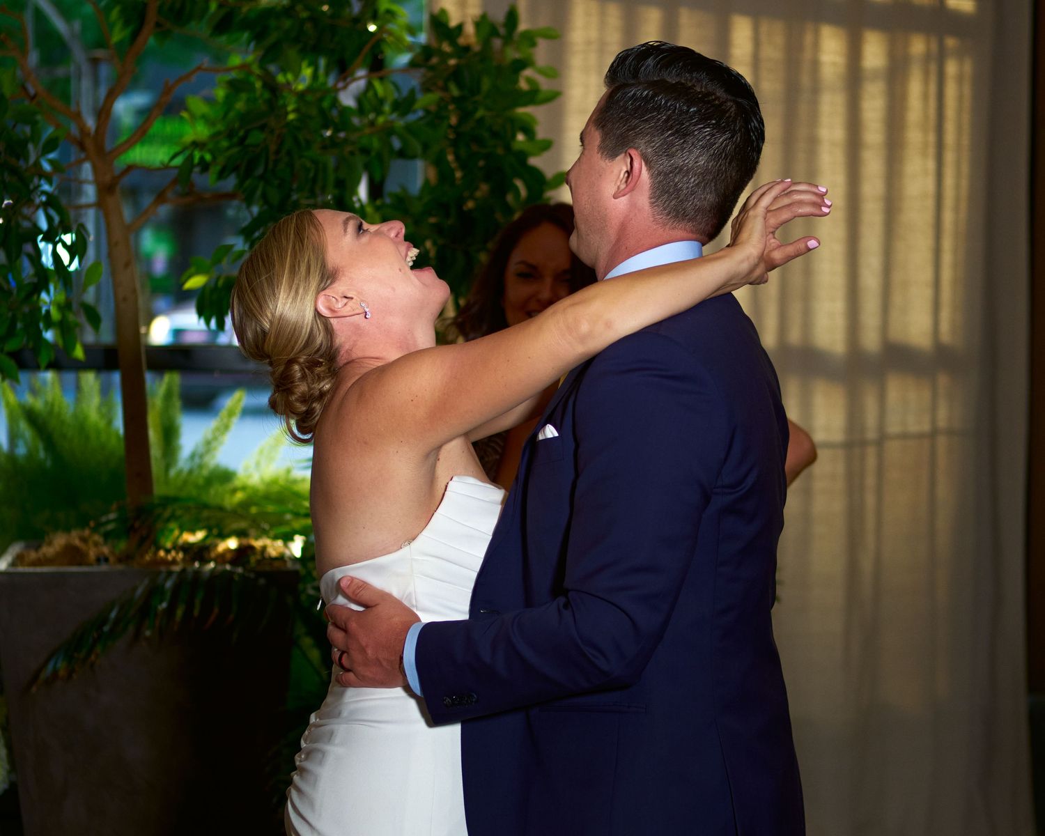 A joyful bride in a white gown raises her arm while embracing her groom in a navy suit during a wedding celebration.