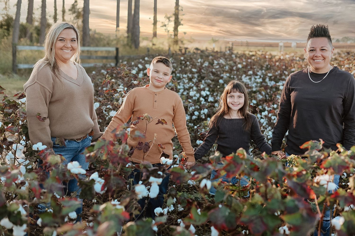 Two women and two children stand together in a cotton field at sunset, smiling with white cotton bolls in the foreground.