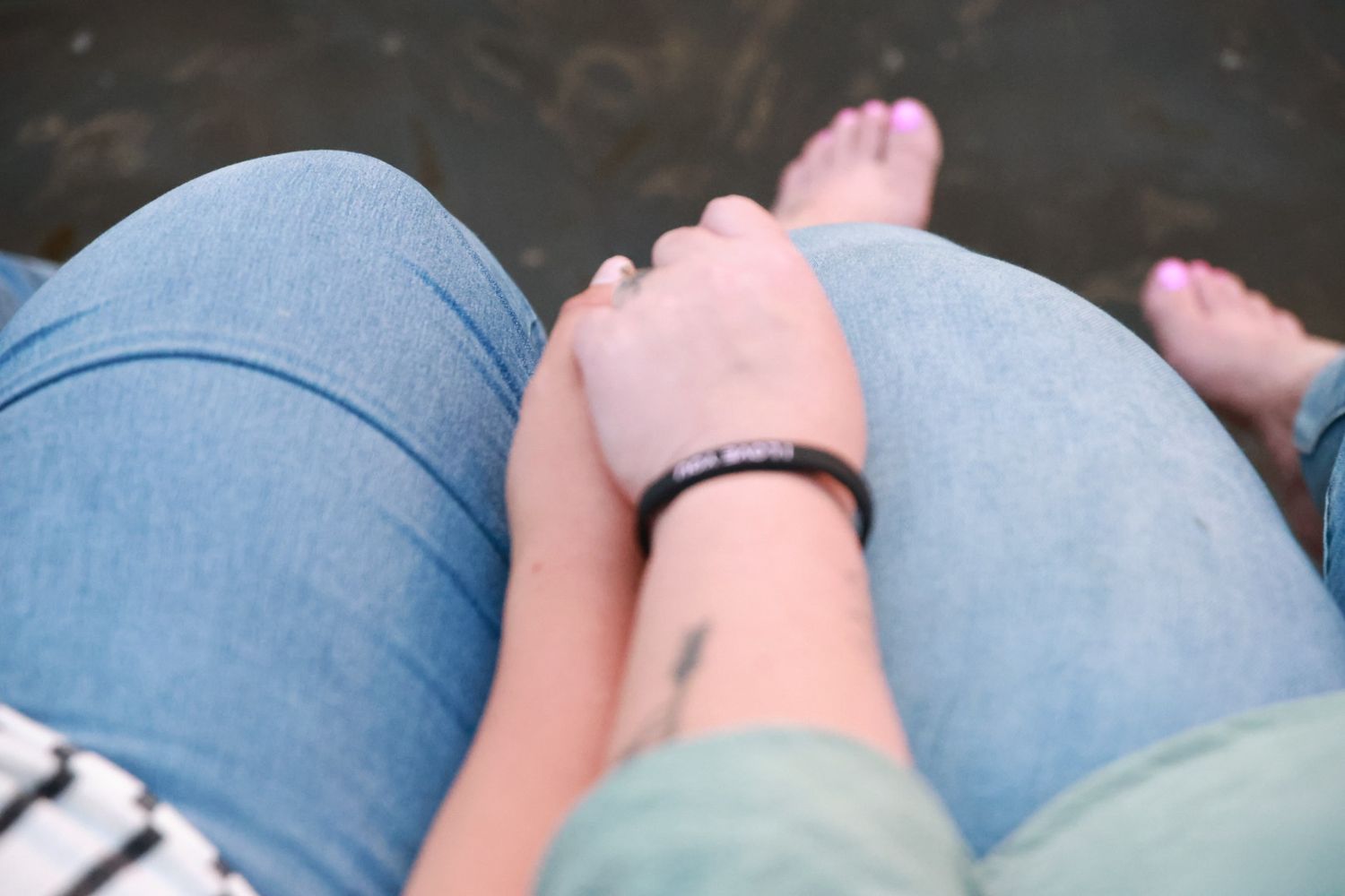 Close-up of two people sitting side by side, one hand resting on a denim-clad knee, with bare feet and pink toenails.