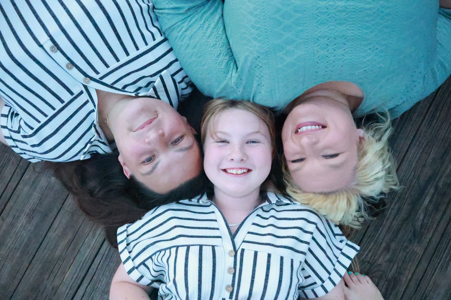 Overhead view of two smiling women and a young girl lying on a wooden dock with their heads together.