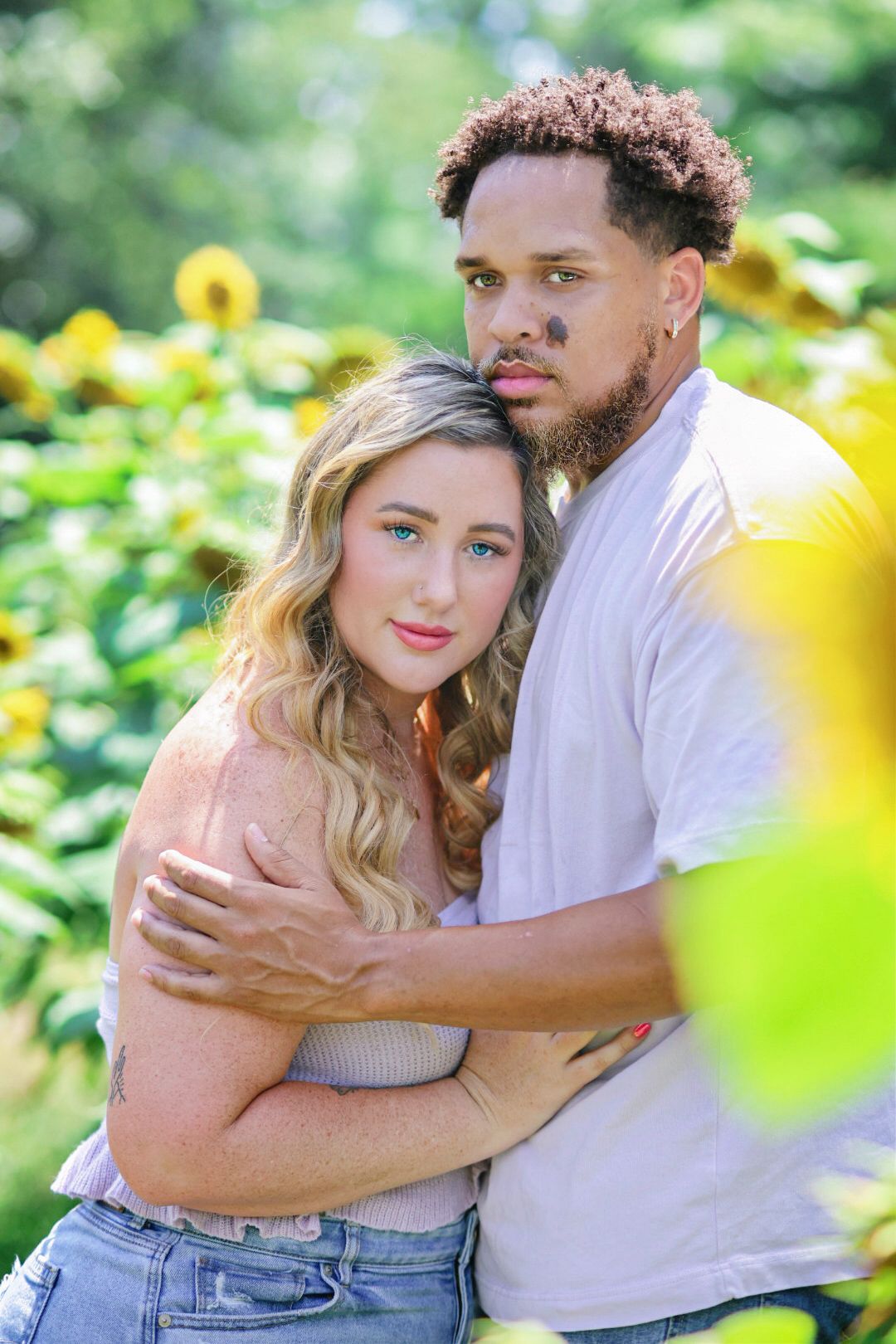 Couple embraces closely in a sunflower field on a bright summer day in a romantic outdoor portrait.