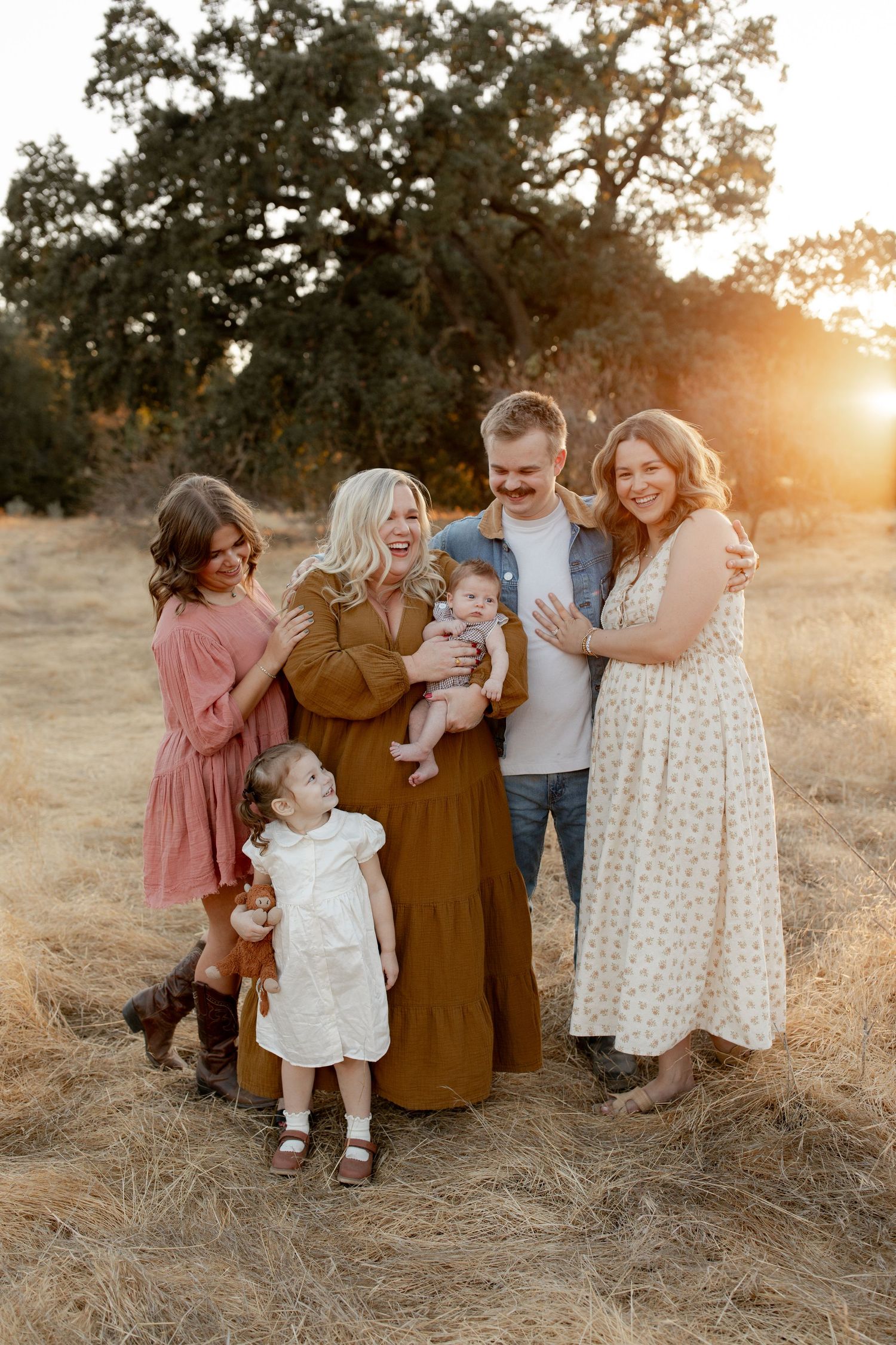 A family shares tender moments together in a golden-lit field at sunset.