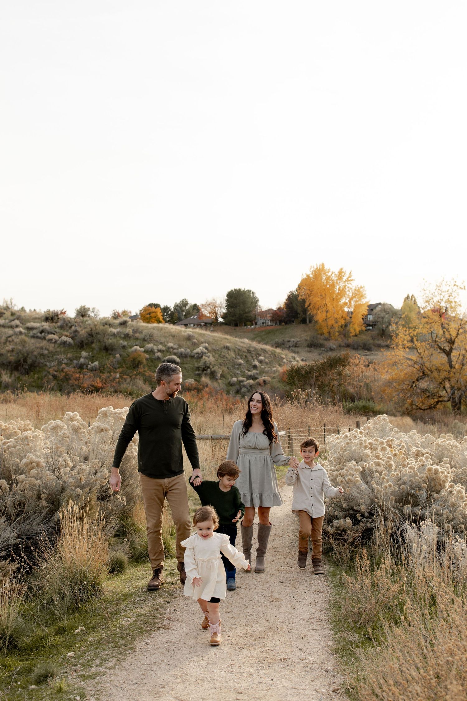 Family of five walking on a dirt path through autumn sagebrush landscape, parents holding hands with children.
