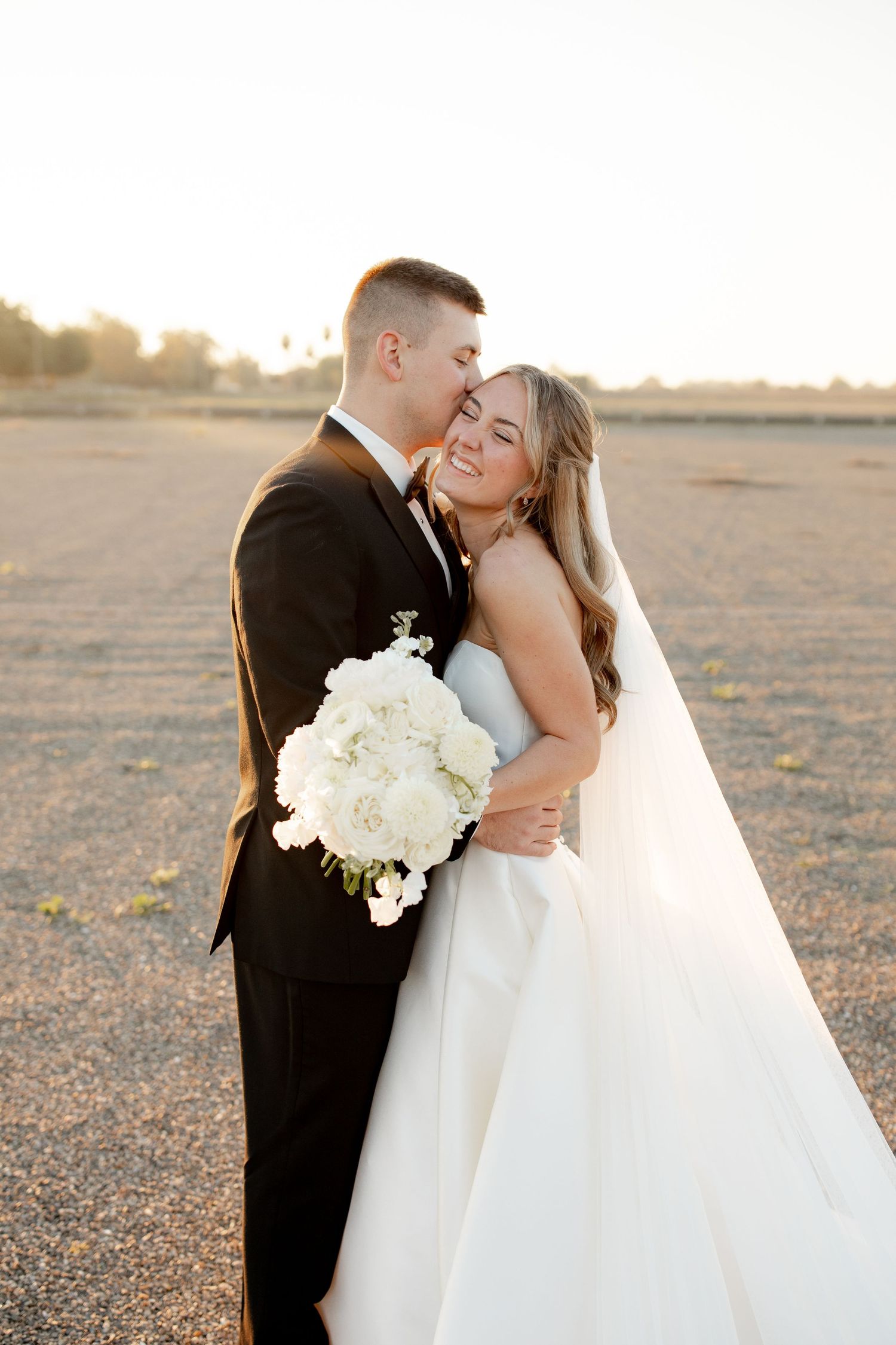 A romantic sunset wedding photo series shows a couple embracing outdoors in formal attire with white flowers.