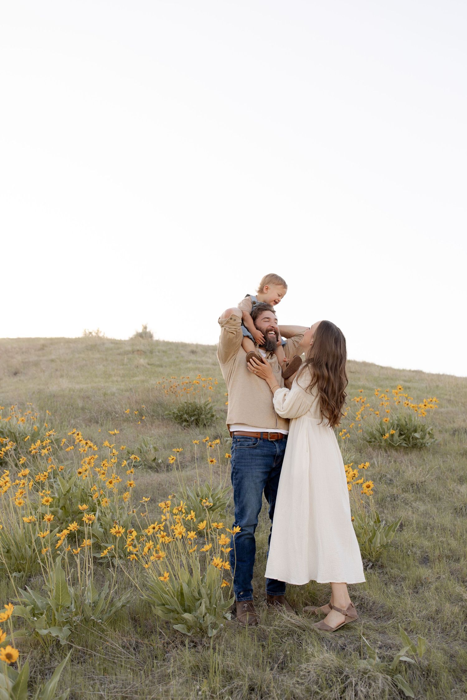 A family shares a tender moment together on a hillside dotted with yellow wildflowers at sunset.
