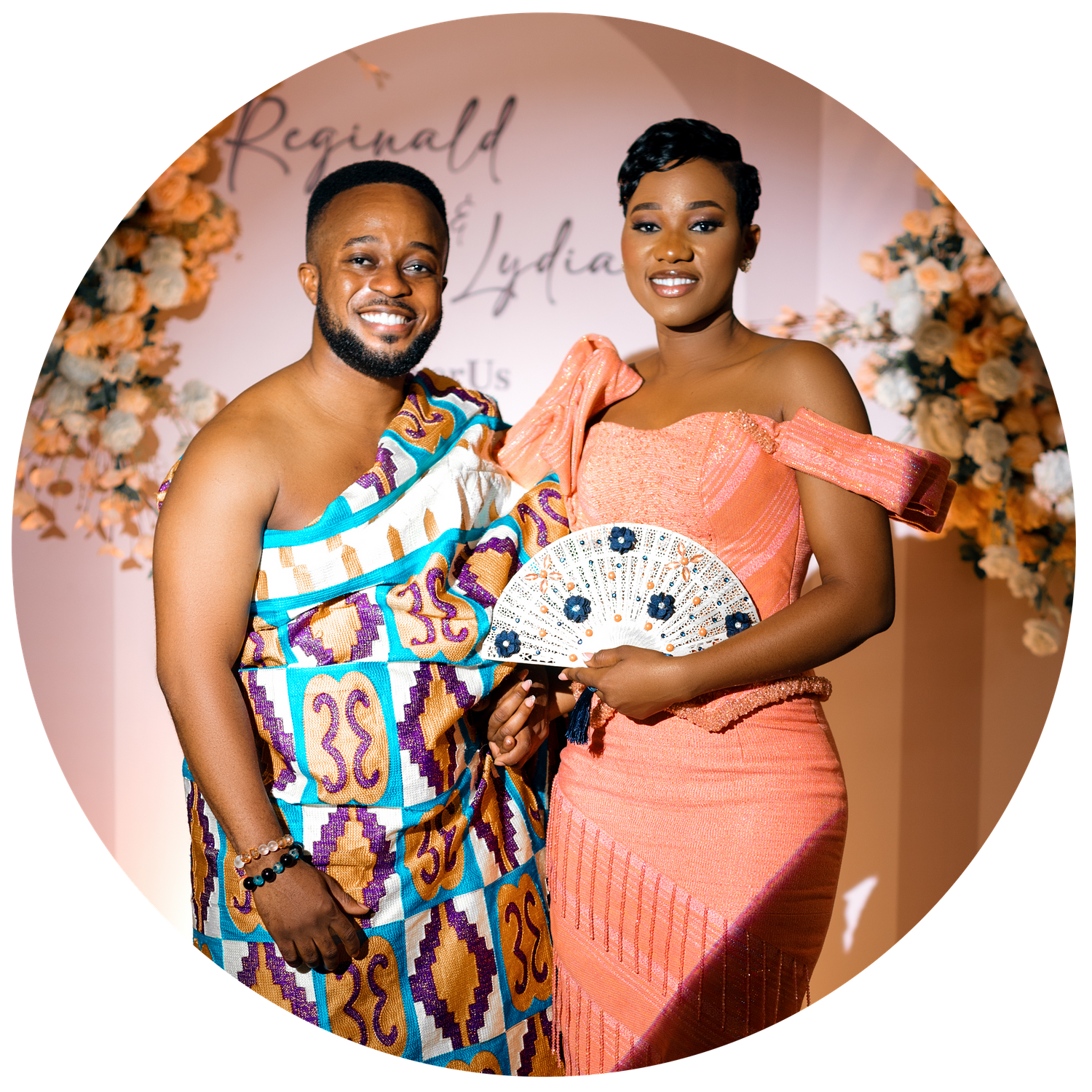 A man and a woman are standing together in front of a decorative floral backdrop.