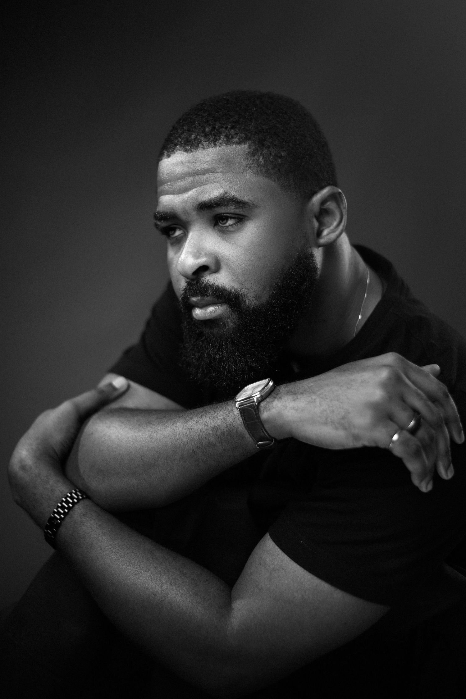A man has his right hand on his left shoulder, wearing a black t shirt and the image is in black and white