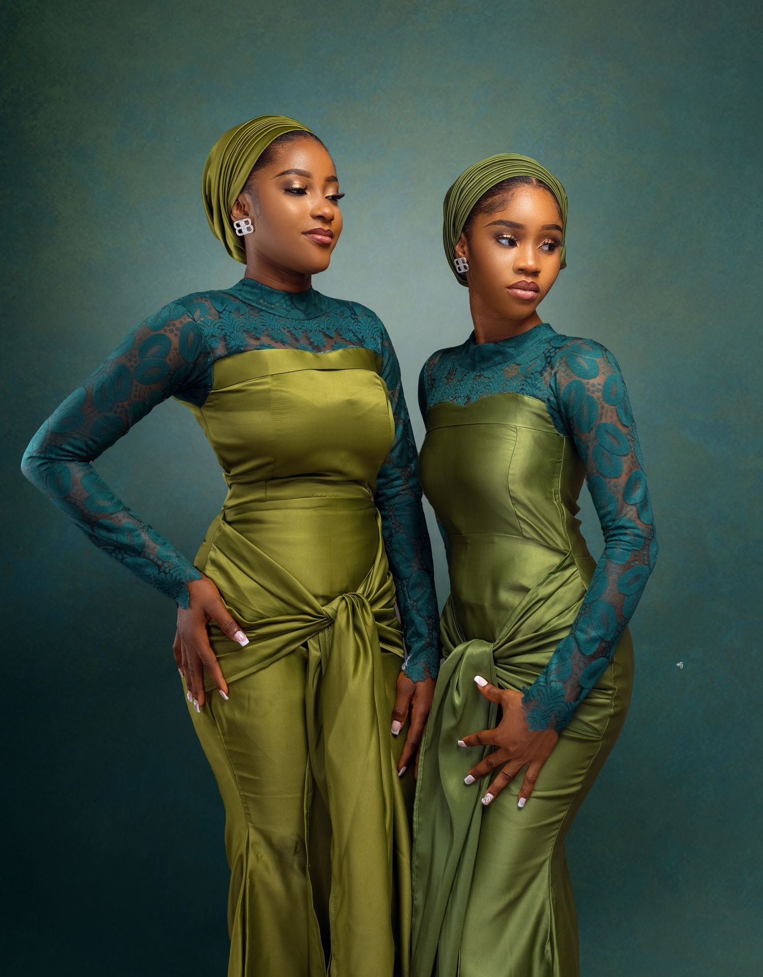 Two women are standing side by side, both wearing matching green outfits with intricate lace sleeves and headwraps. They are posing with one