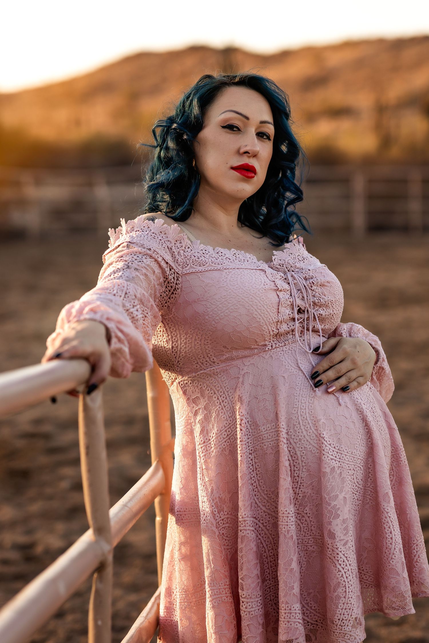A vintage-inspired maternity portrait features a pink lace dress against a desert landscape.
