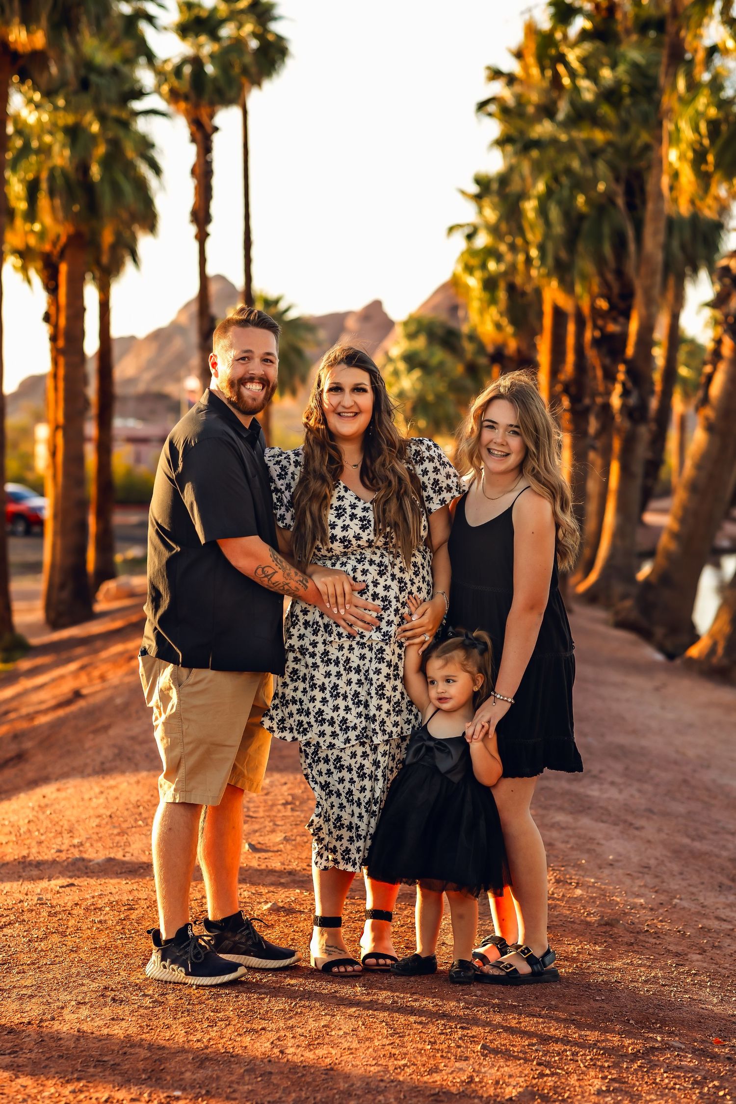 Family portrait at sunset with palm trees lining a desert road in warm golden light.