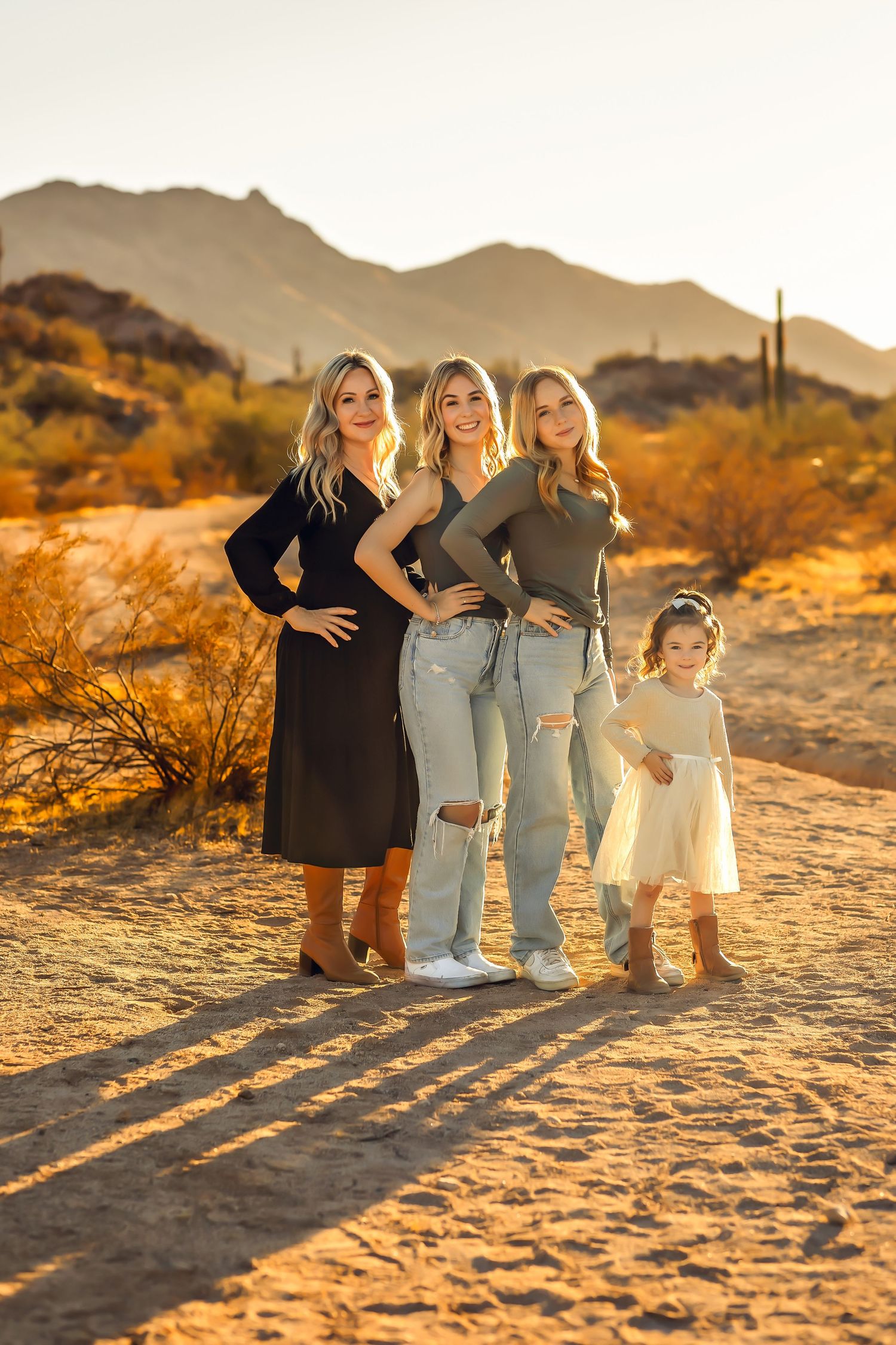 A group poses together in the desert at sunset with mountains and saguaro cacti visible in the golden background.