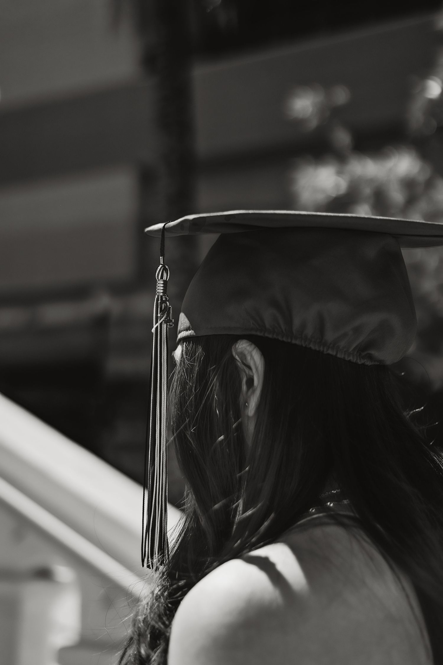 Close-up side view of graduation cap with tassel in dramatic black and white lighting.