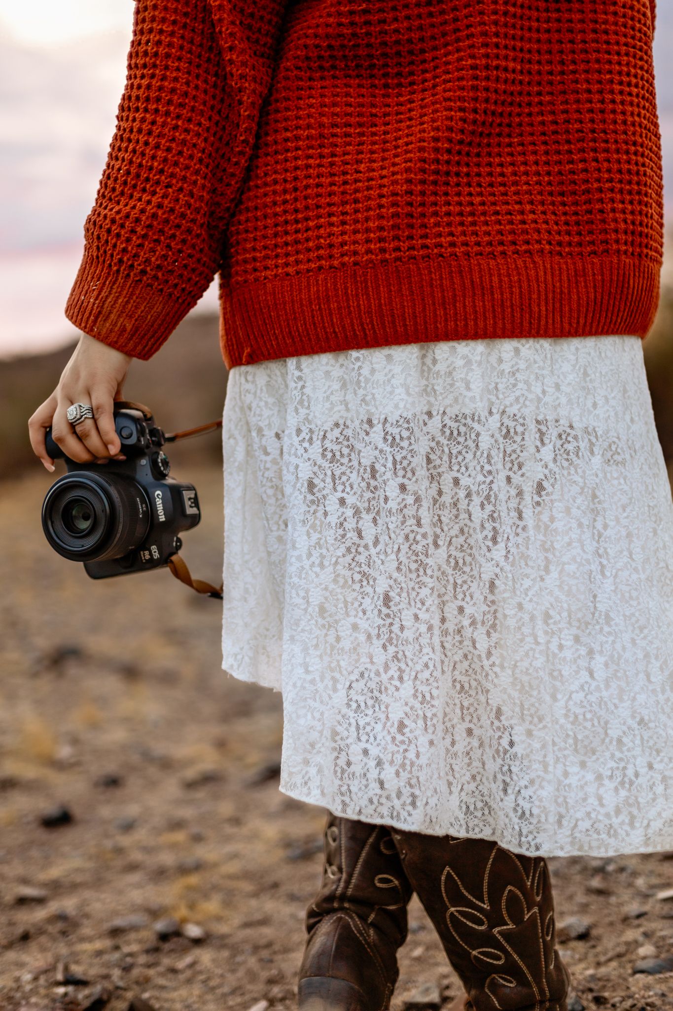 Close-up of red knit sweater, white lace dress, and camera in desert setting.