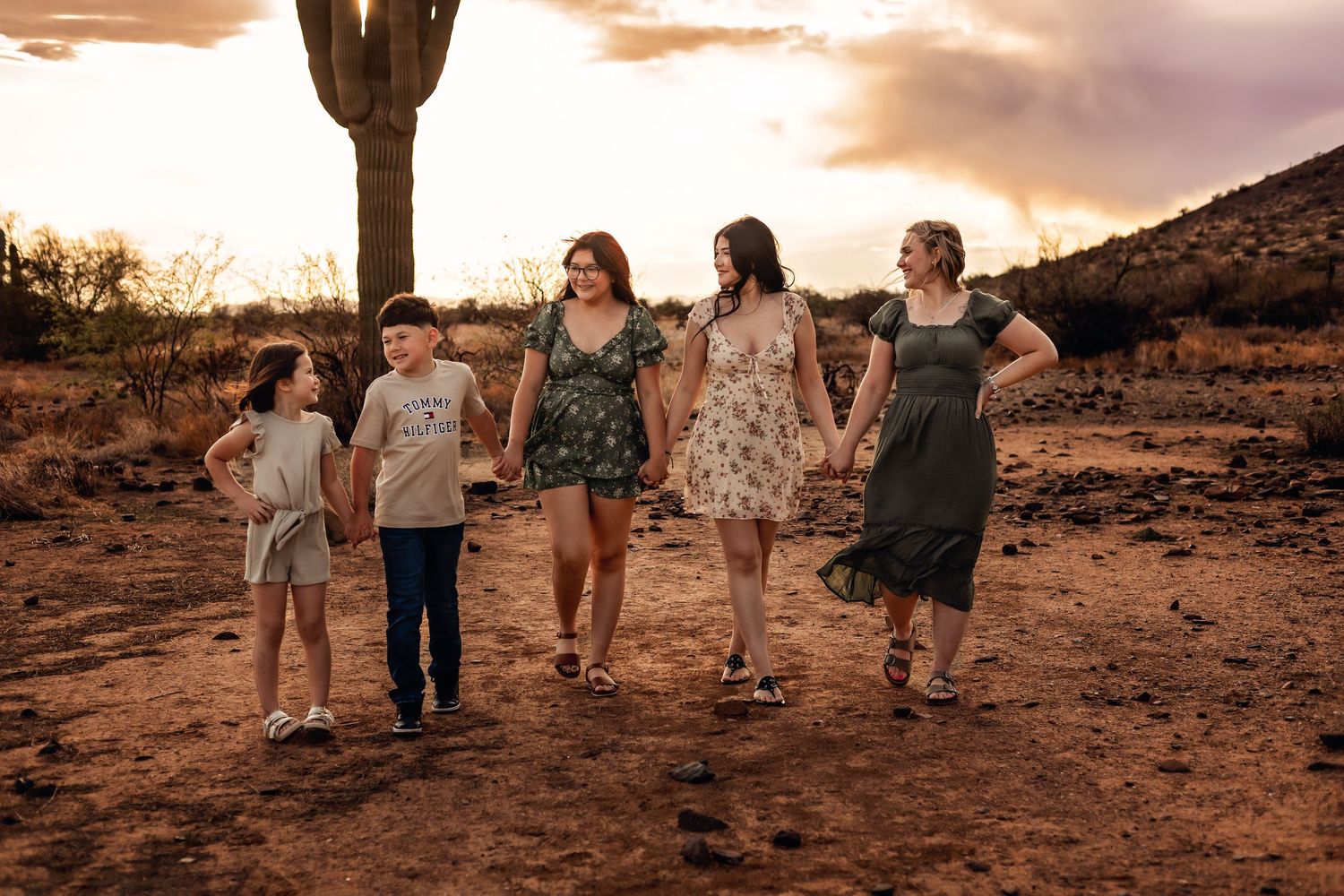 A group walking together at sunset in a desert landscape with saguaro cacti silhouetted against dramatic sky.