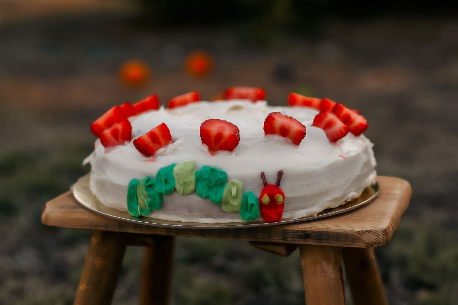 A decorated white birthday cake with red and green accents displayed on a wooden stool.