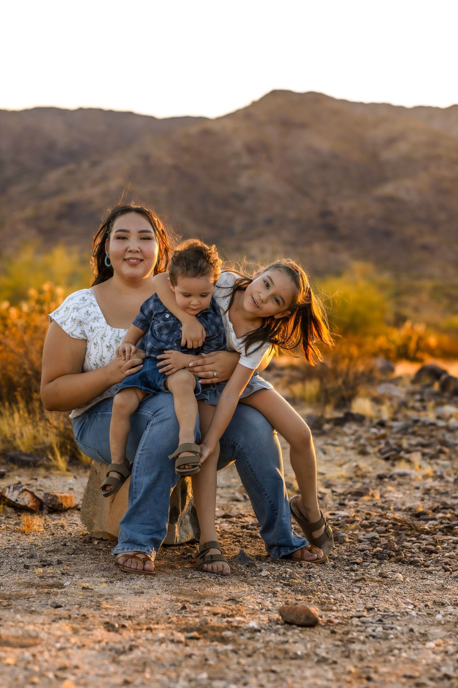Three people share a joyful moment together against a desert mountain backdrop at sunset for their family session in Buckeye.