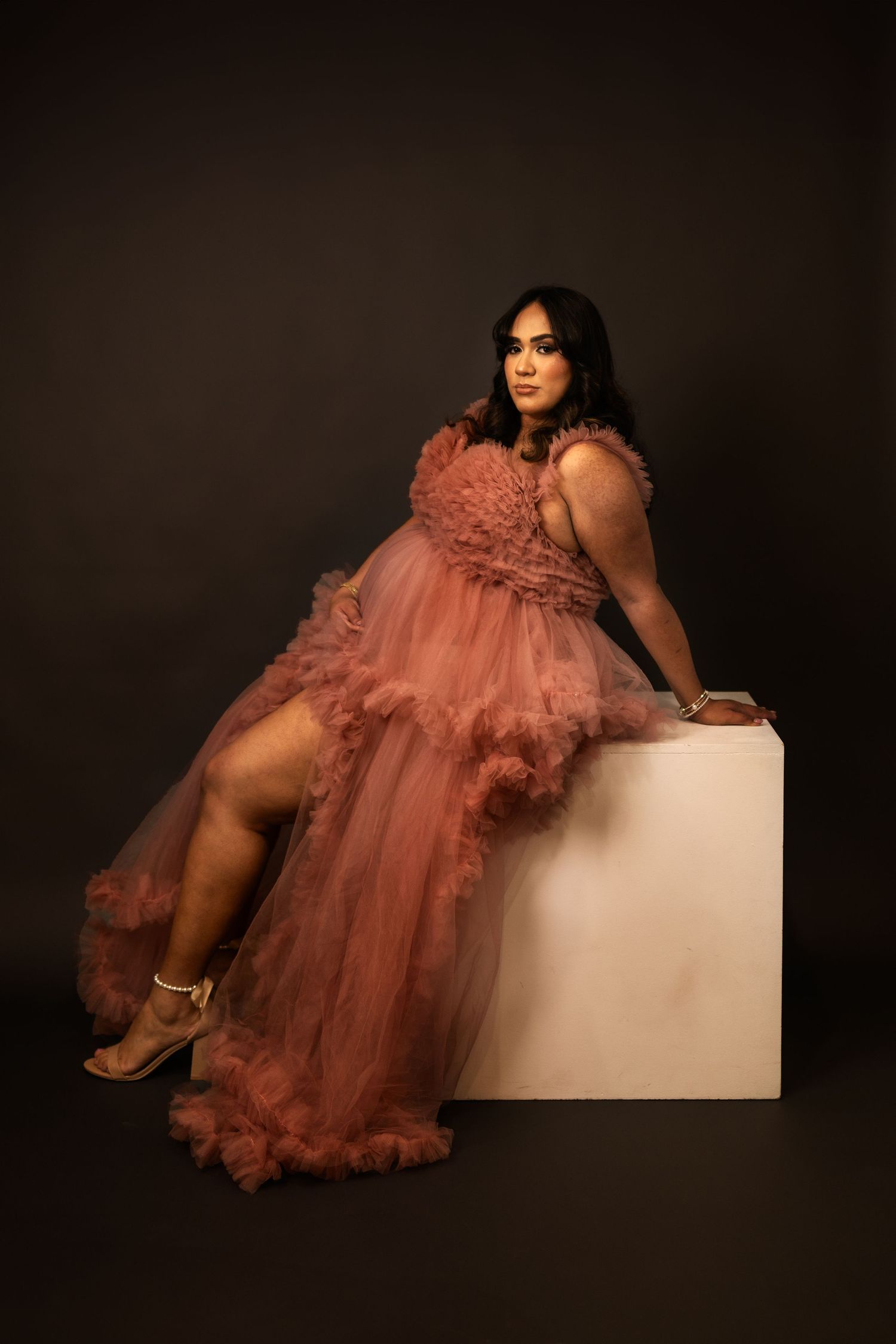 A dusty rose tulle gown creates a dramatic maternity portrait against a dark studio background in Goodyear.