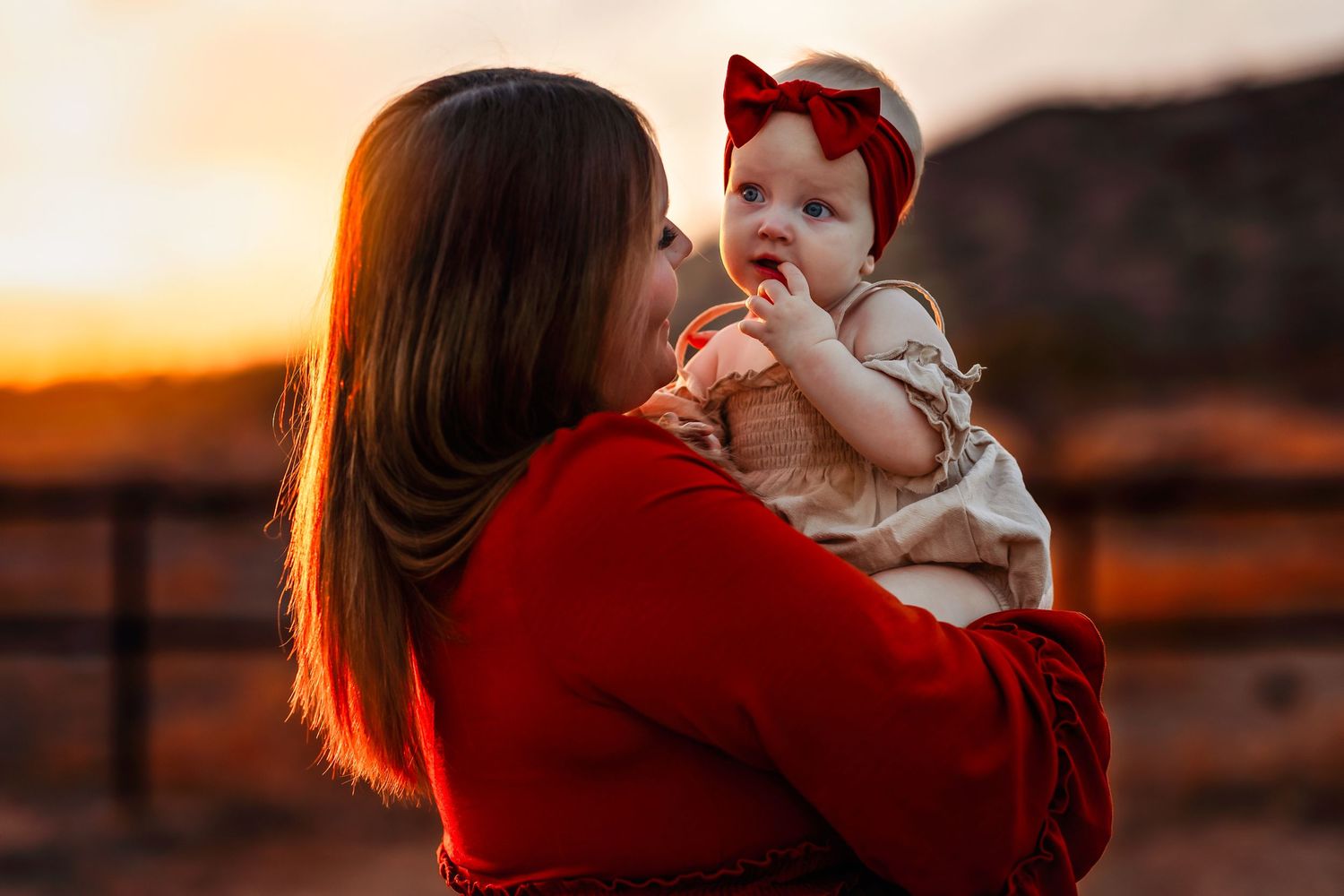 Mother and baby share tender moment in front of sunset mountain landscape in Arizona.