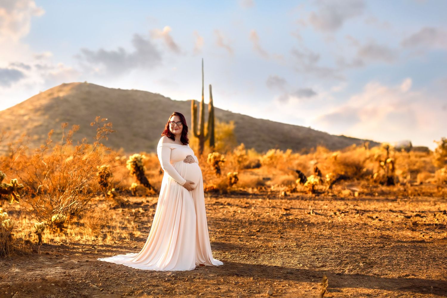 Woman in flowing white dress poses in desert landscape during golden hour.