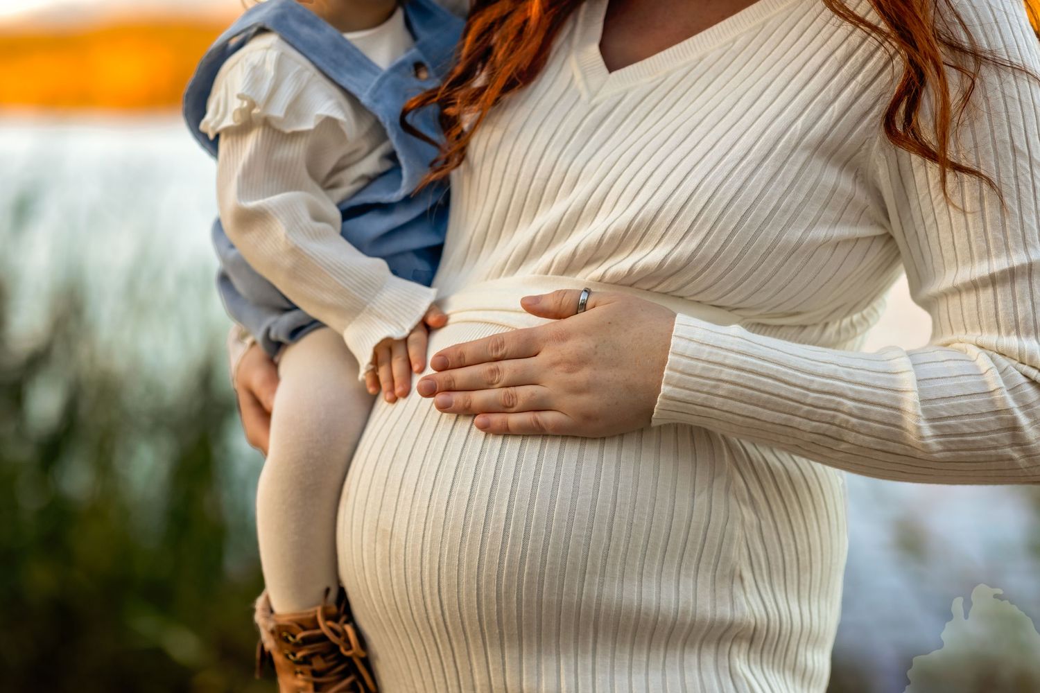 Close-up of a pregnant woman in a cream sweater with hands resting on her baby bump.