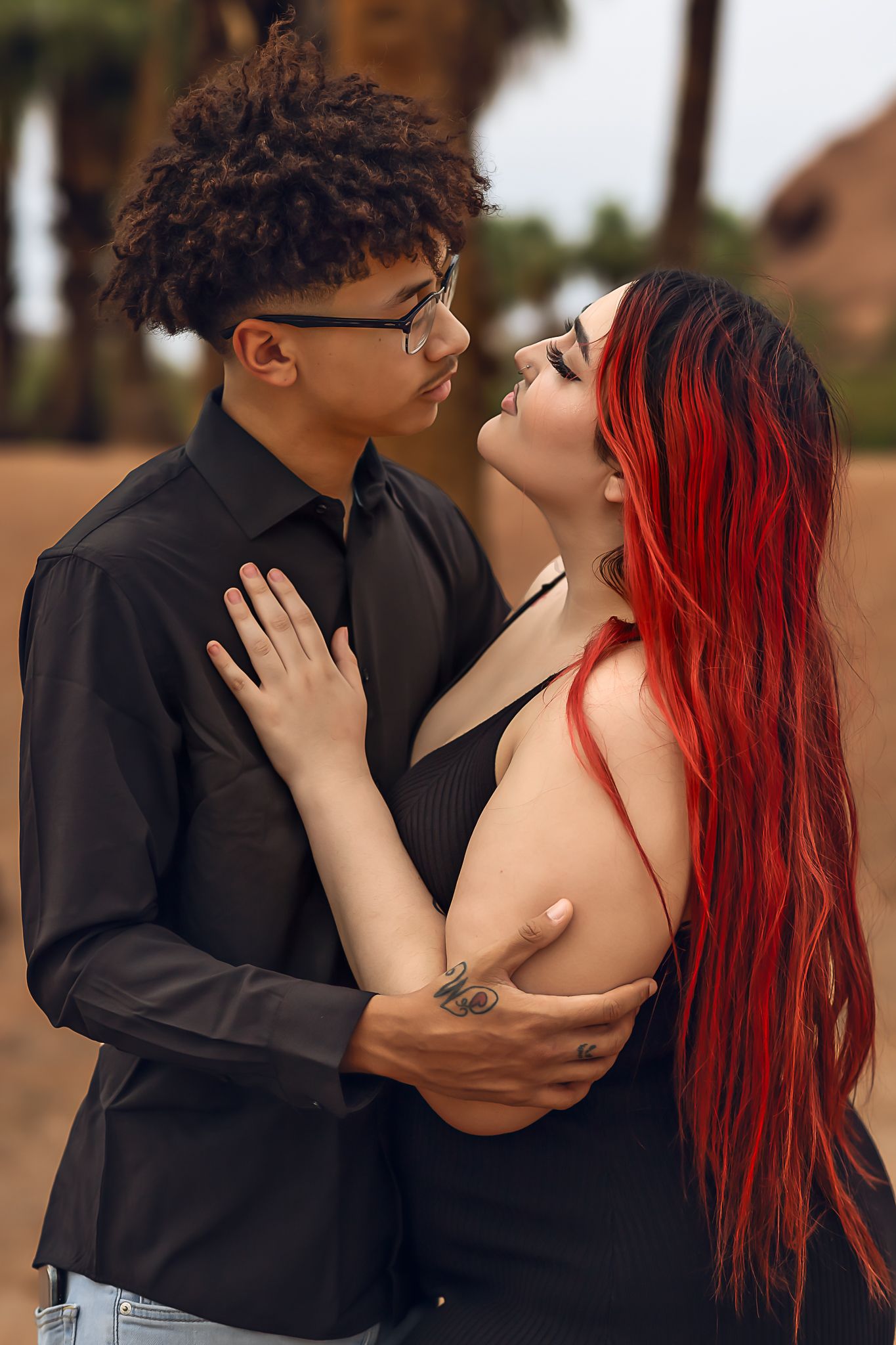 A romantic couple in black and red attire embrace in an intimate outdoor photoshoot.