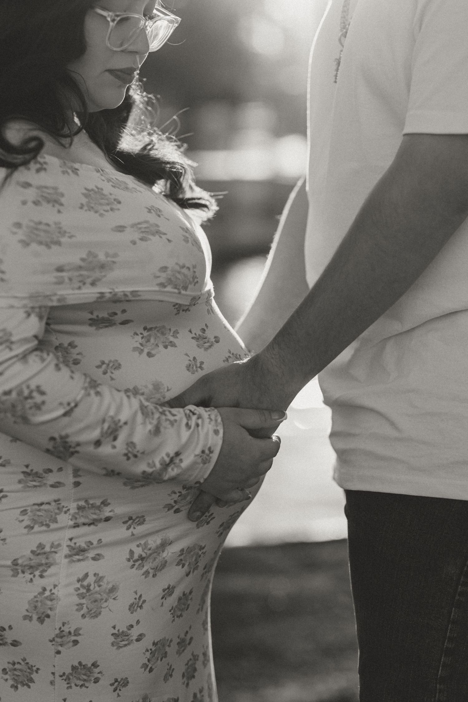 A black and white intimate maternity photo captures hands resting on a pregnant belly.