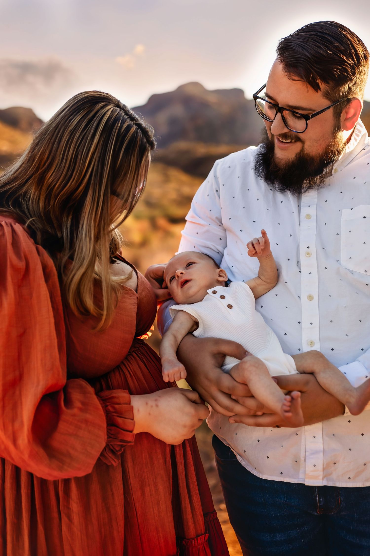 A tender family moment captured at sunset in a desert landscape with parents admiring their infant child.