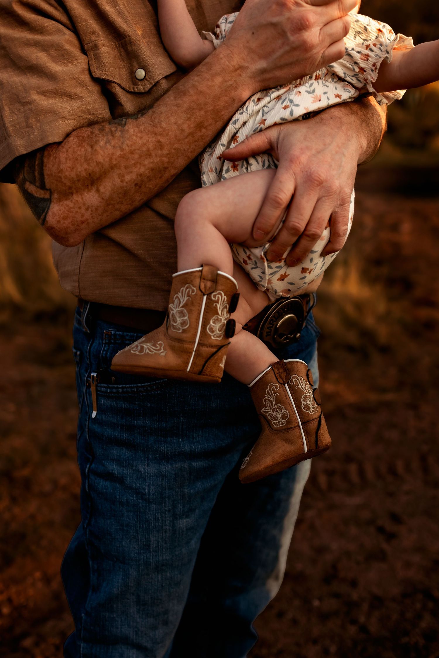 Close-up of tiny brown cowboy boots on small feet while being held against denim jeans and brown jacket.