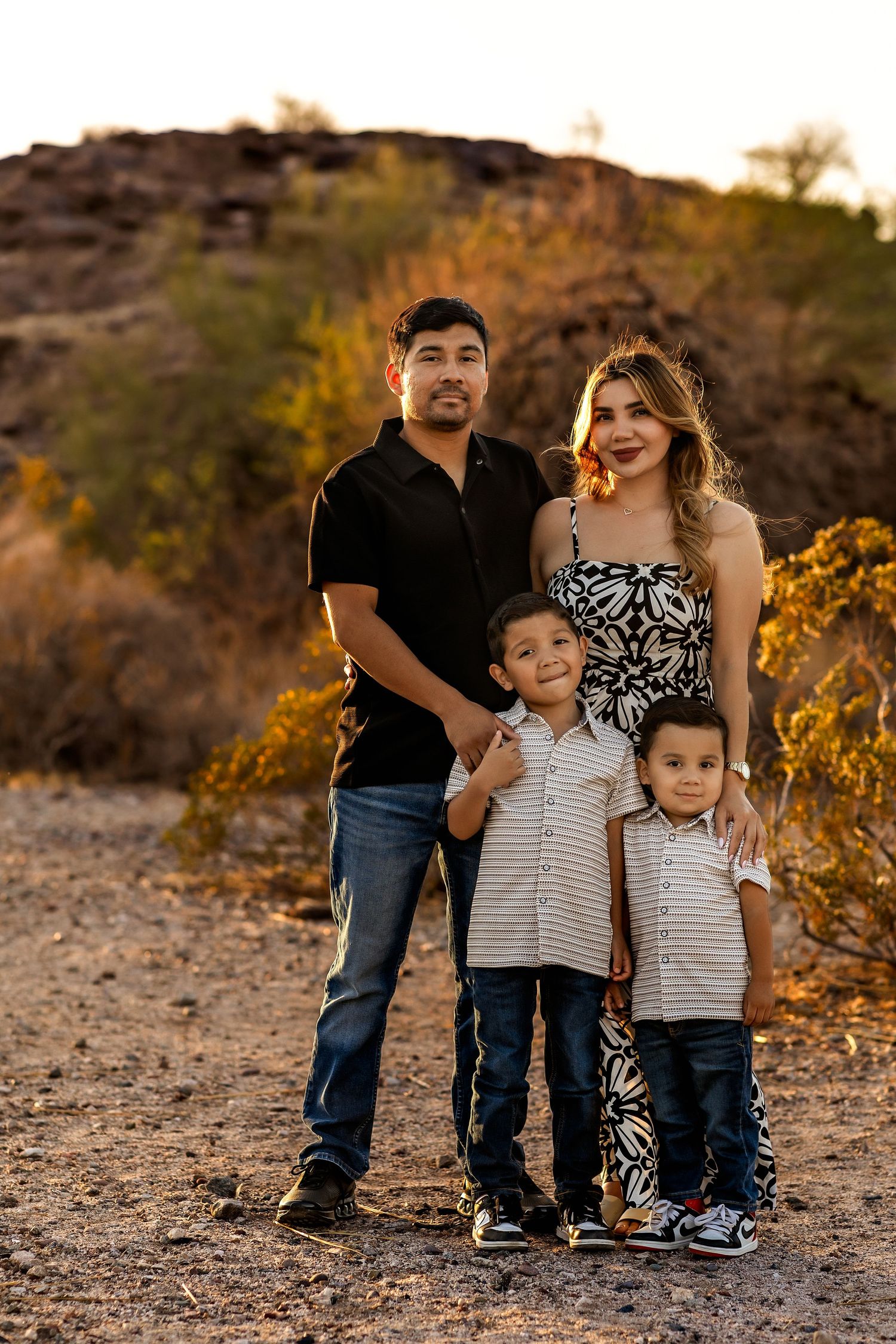 A family of four poses together on a desert trail at golden hour with mountains in the background.