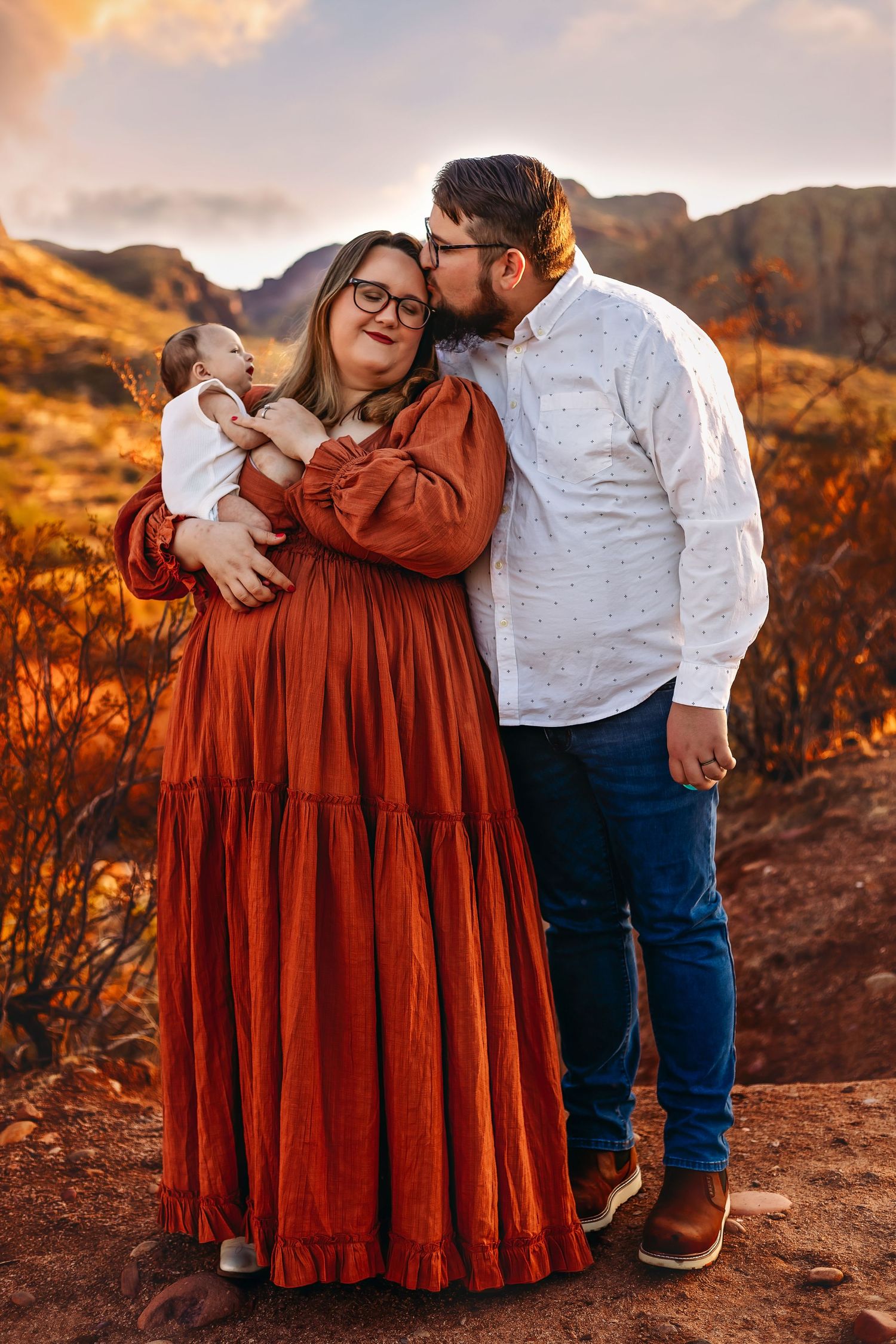 A couple embraces in warm sunset light against desert mountains, wearing rustic autumn-colored clothing.