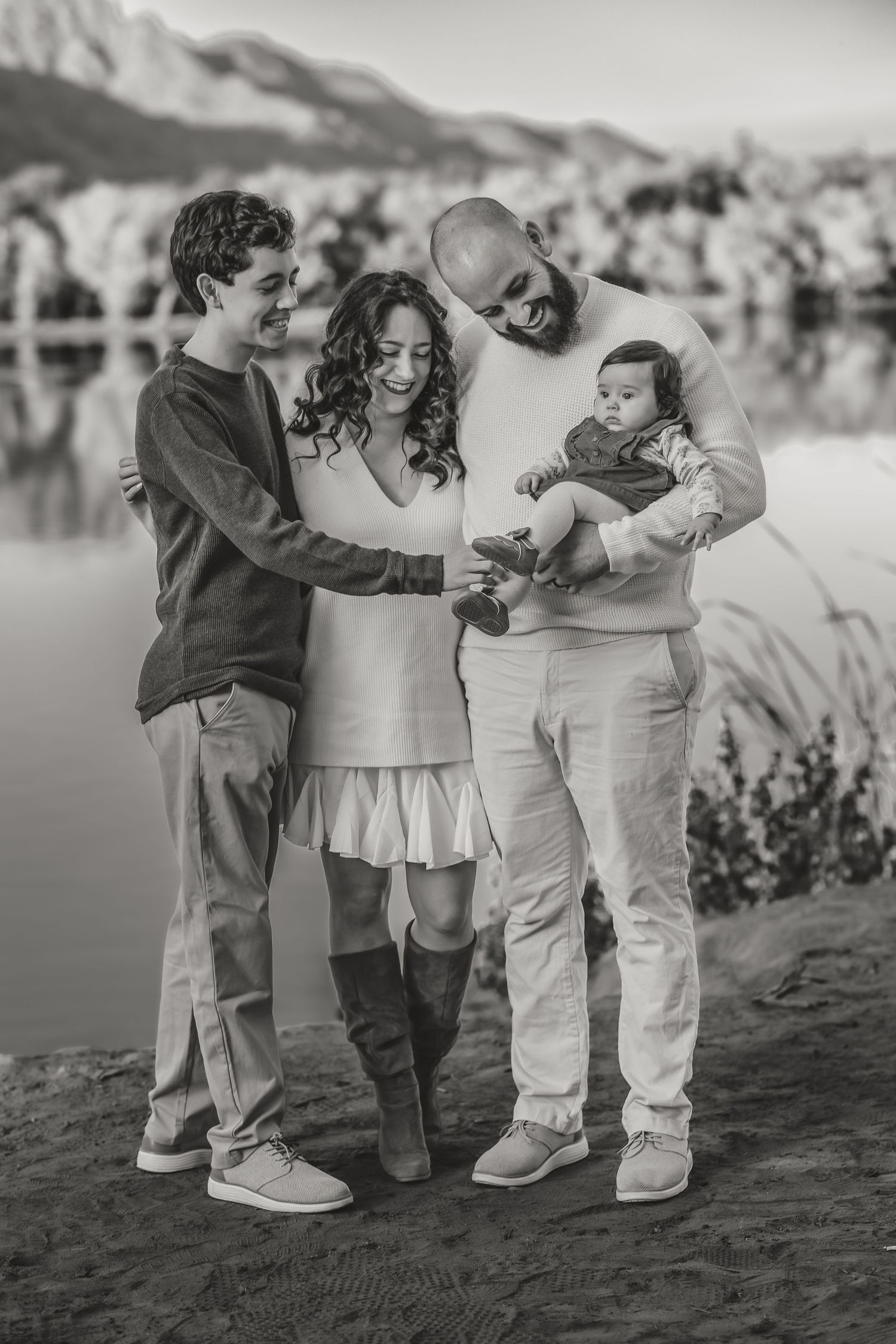 A family shares a tender moment by a lake with mountains in the background.