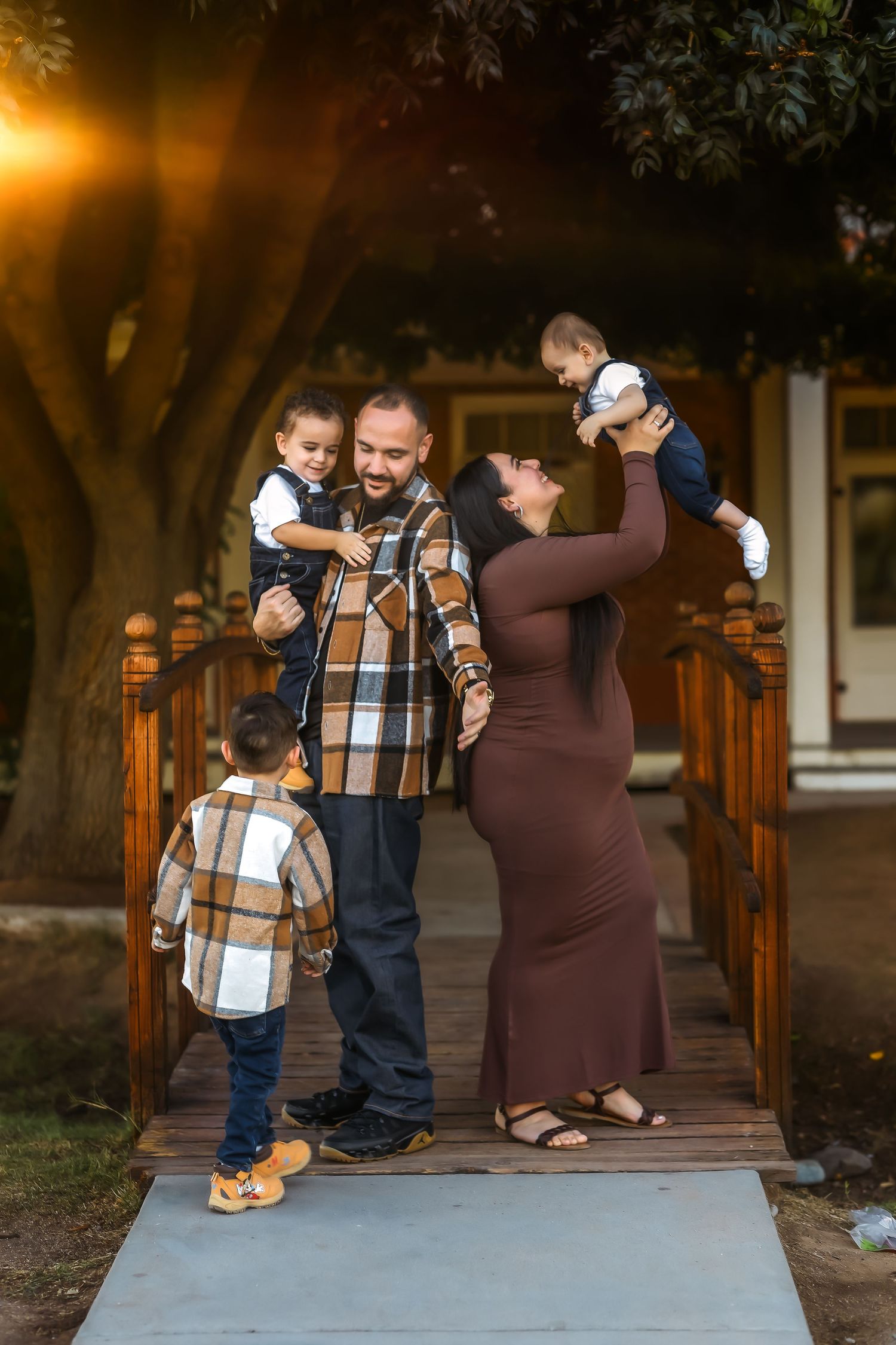 A family of five poses on a wooden bridge, with parents holding young children in casual fall attire.