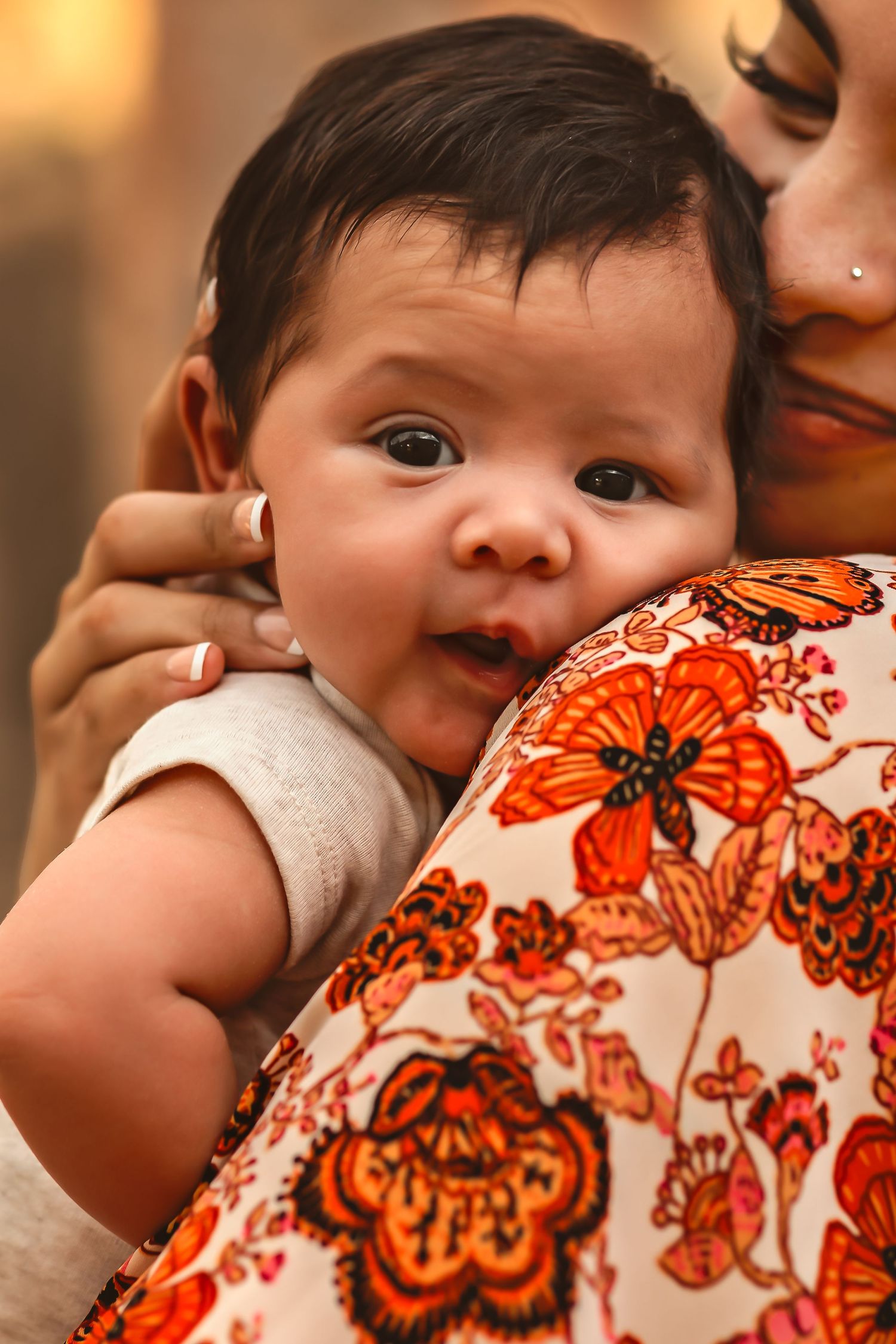 A baby in white onesie rests against a floral orange patterned fabric in warm lighting for newborn photo session.