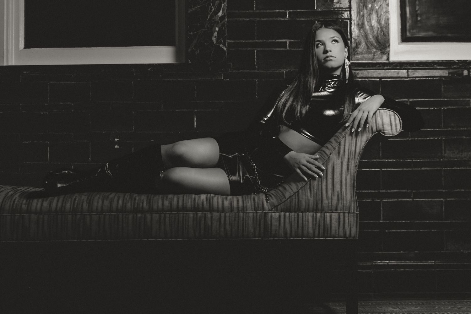 Black and white vintage photograph of a person reclining on a striped couch near a brick wall.