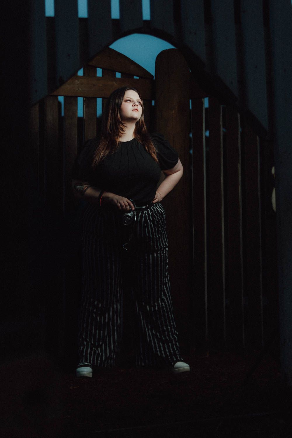 Moody portrait in dark setting with striped pattern dress casting dramatic shadows and lighting effects.